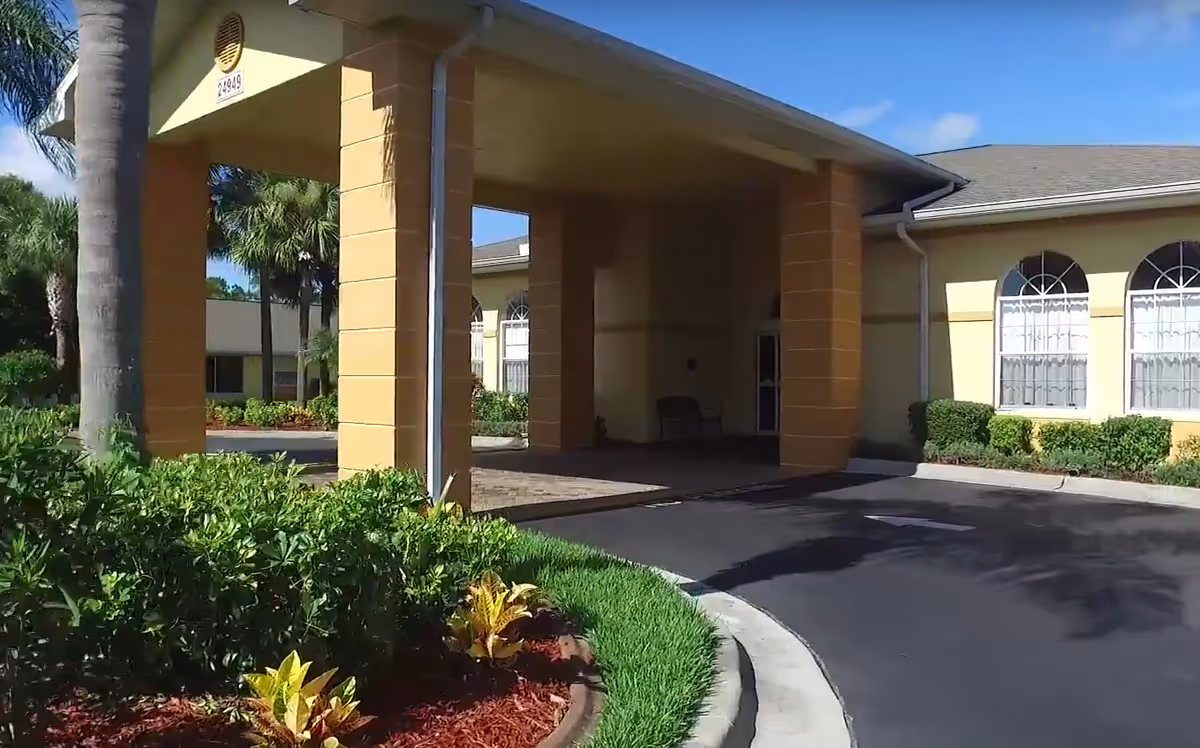 Front entrance porte-cochere of a single-story yellow building with landscaping and a curved driveway.