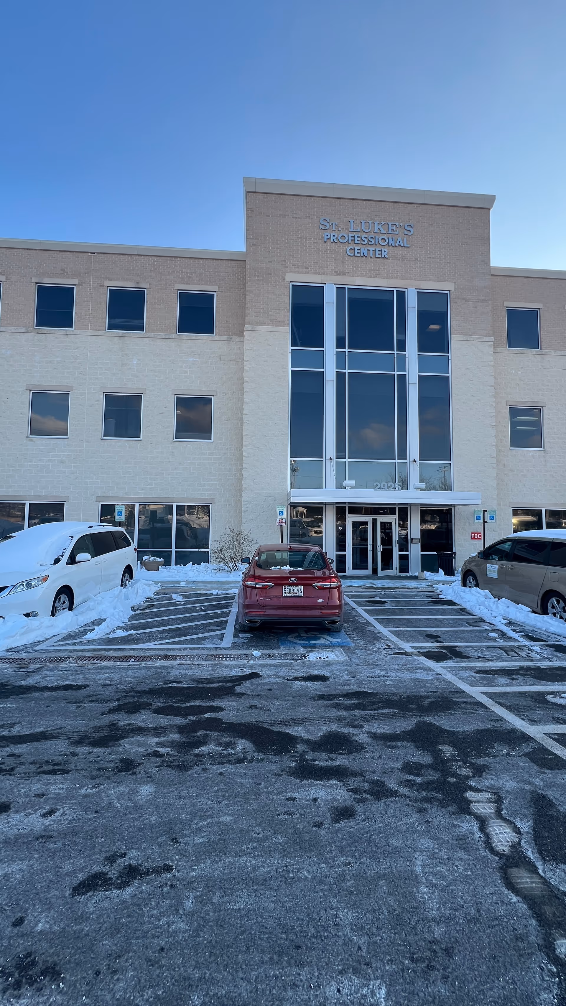 Modern medical center with glass entrance and snow-covered parking lot.