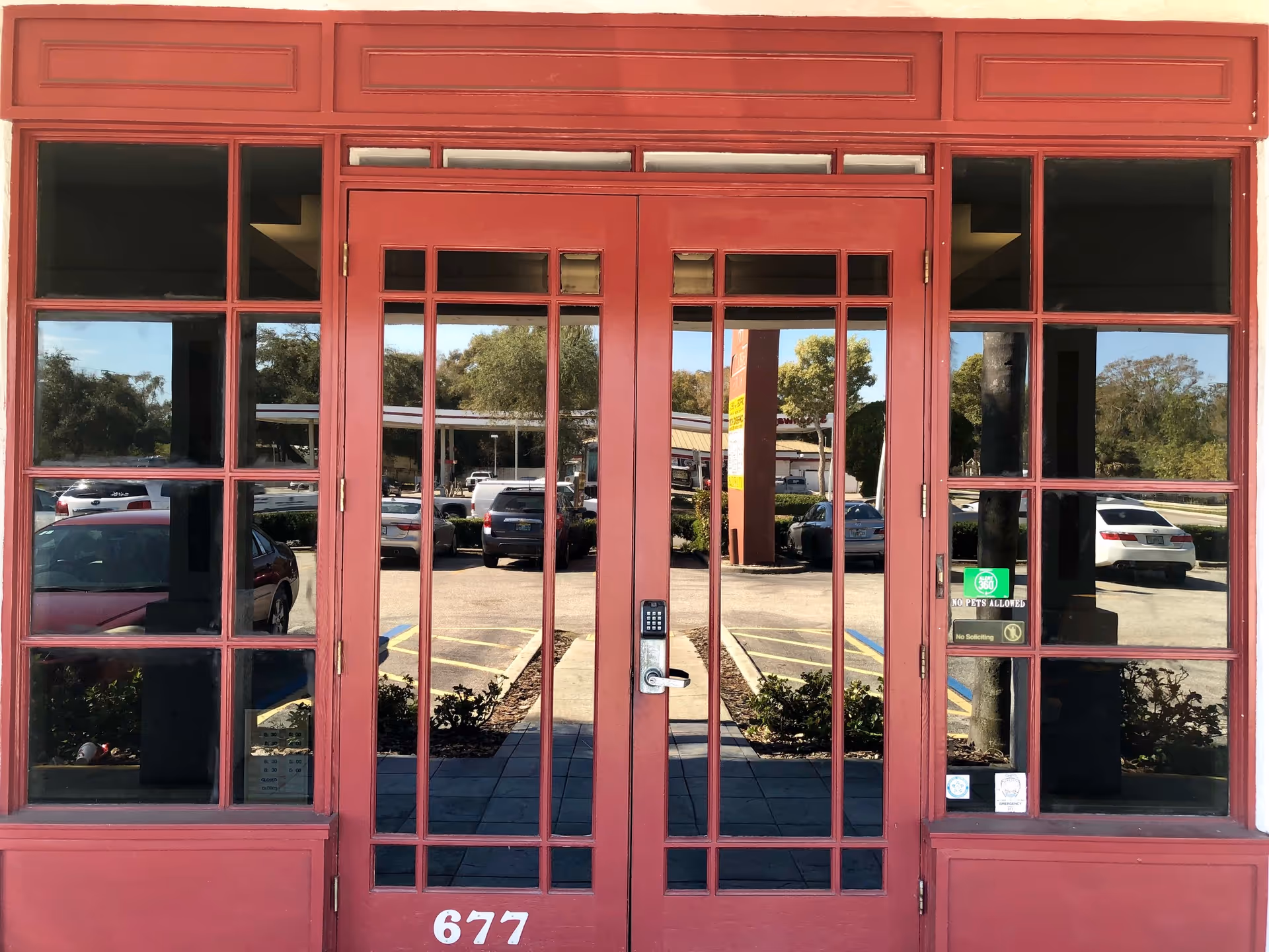 Red framed glass doors and windows frame the building entrance, with a parking lot visible outside.