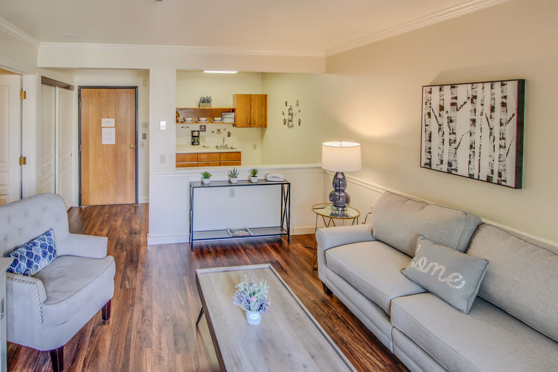 Cozy living room with gray sofa, armchair, coffee table, and open kitchen pass-through.