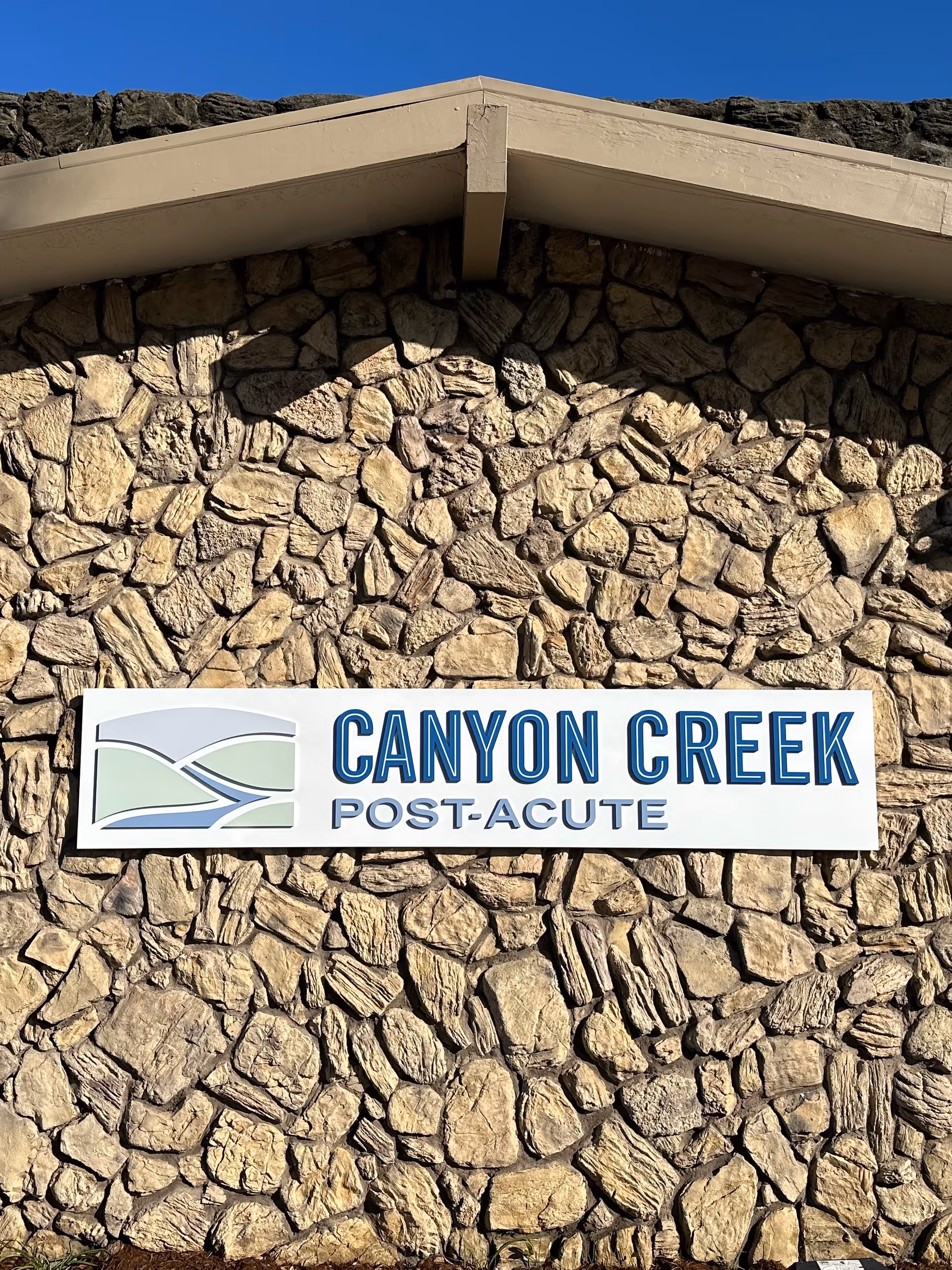Stone wall exterior with a Canyon Creek Post-Acute sign under a sloped roof