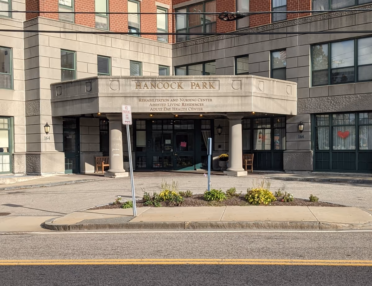 Exterior view of Hancock Park Assisted Living entrance with columns and landscaping.