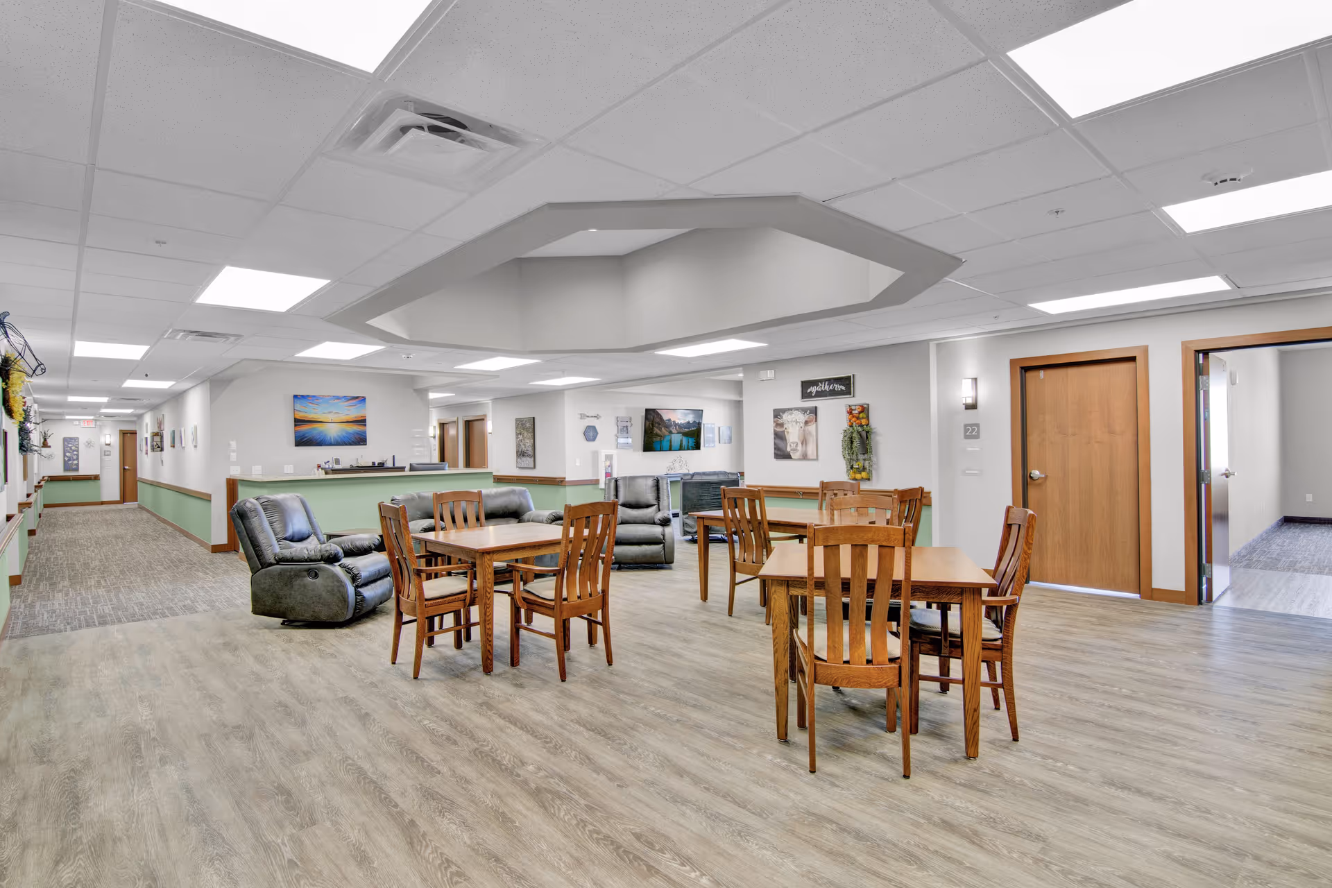 A spacious senior living common area with wooden tables, chairs, and recliners.