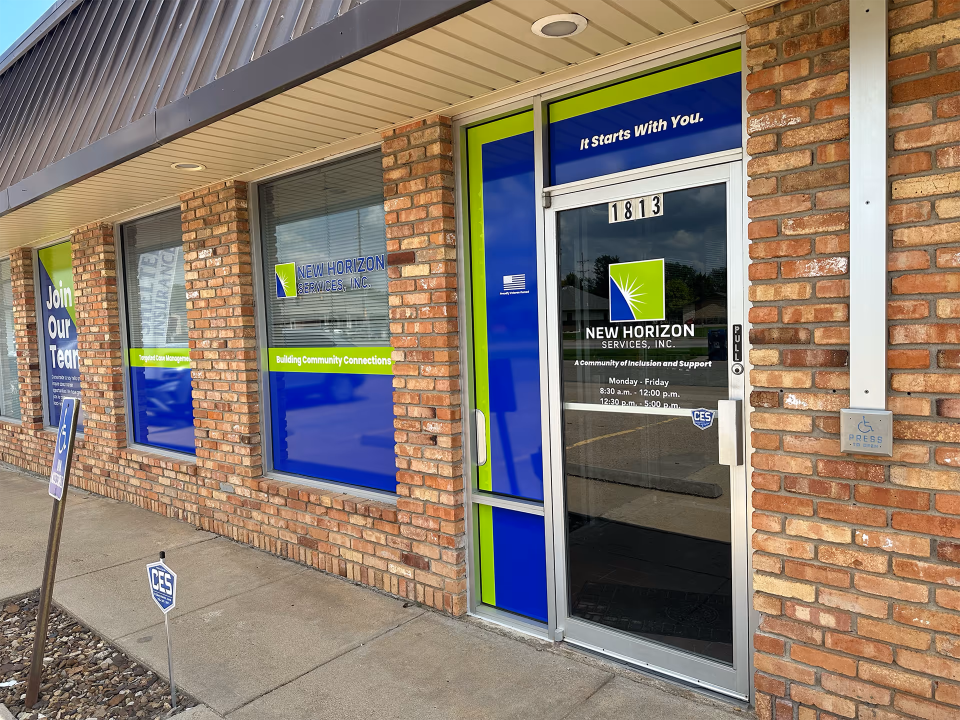 Brick storefront with blue and green signage for New Horizon Services and a glass door.