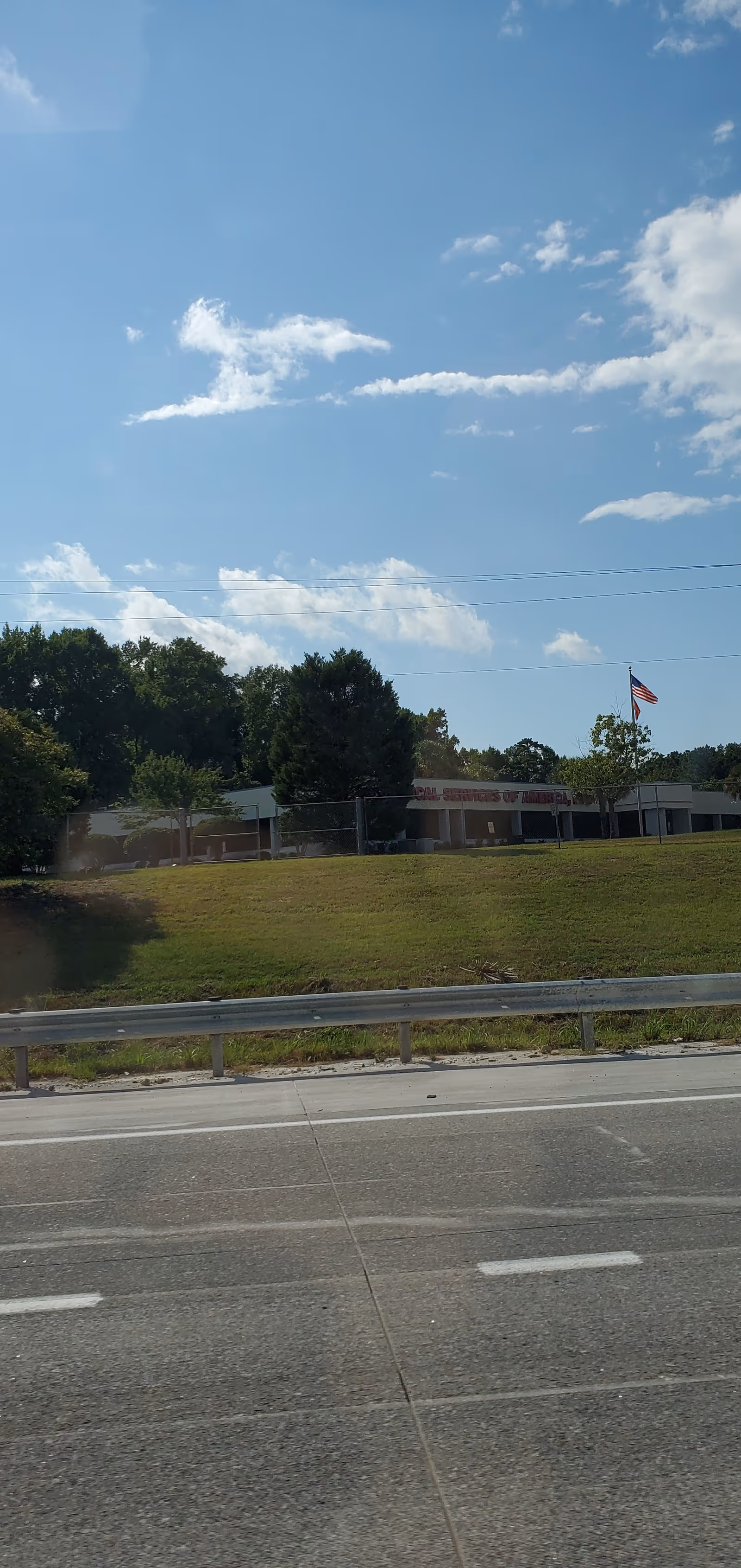 A road in the foreground, grassy slope, and a low, single-story building with an American flag.