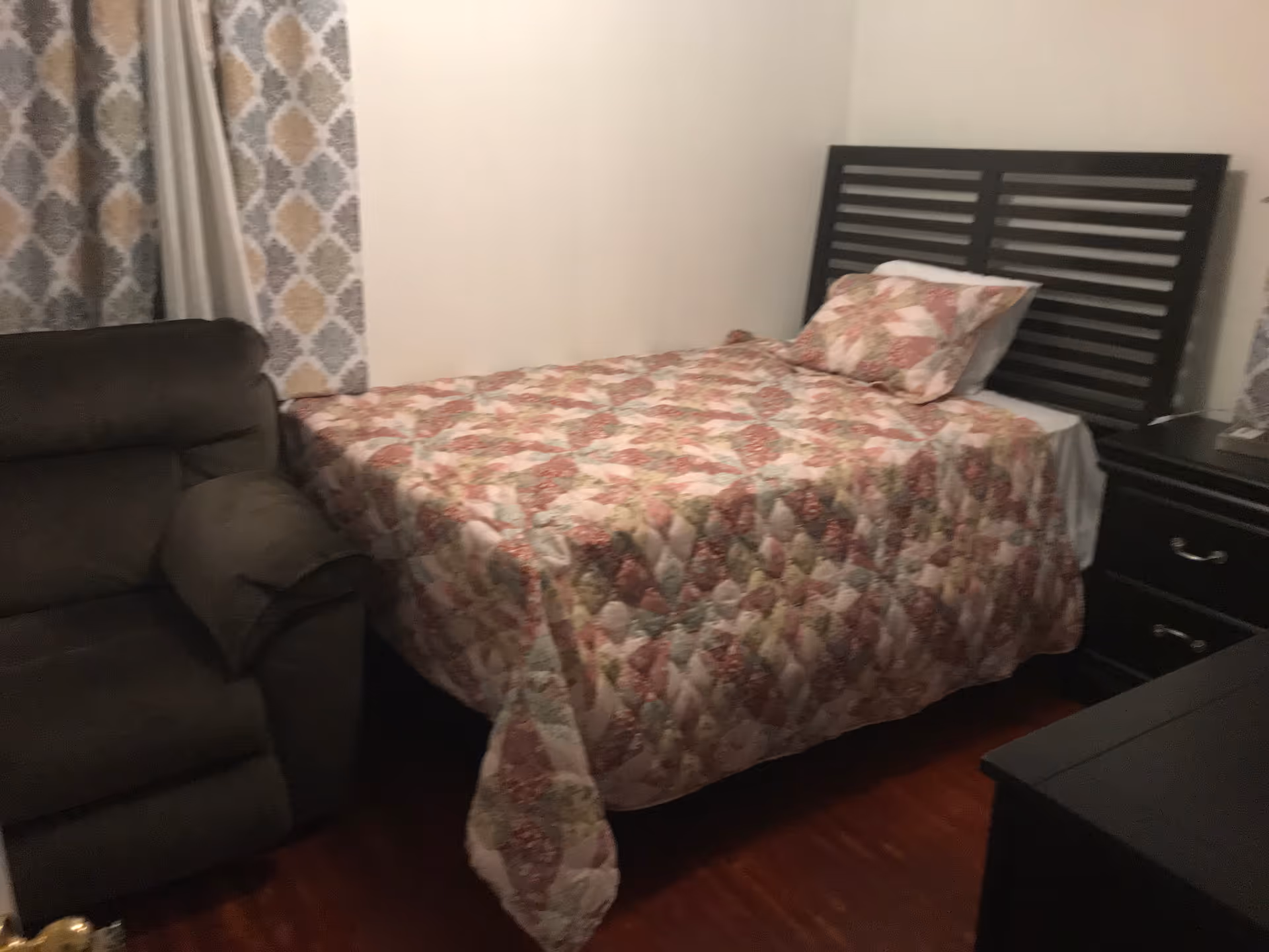 A cozy bedroom with a floral quilt, headboard, and dark wood furniture.