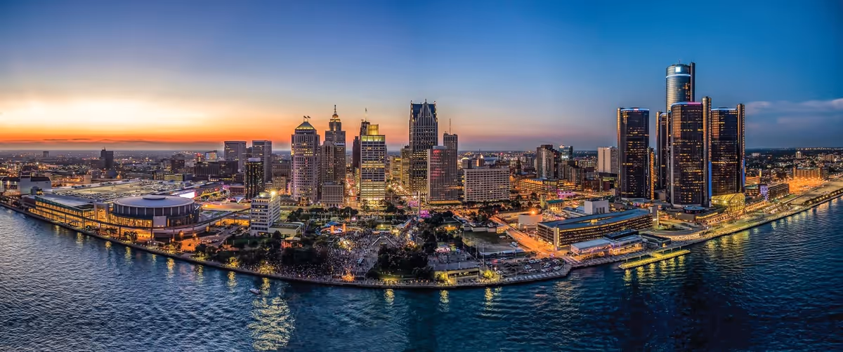 Panoramic city skyline along a river at sunset with illuminated skyscrapers