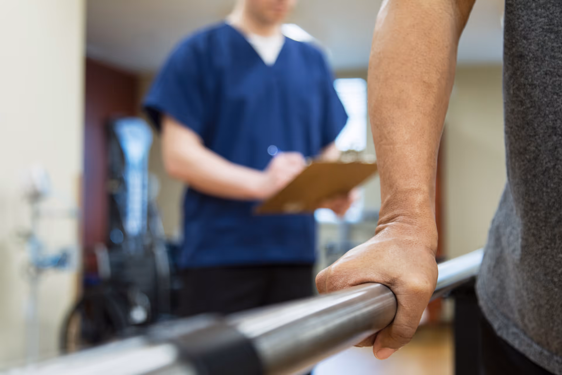 Close-up of a hand gripping a railing while a medical professional appears blurred in the background.
