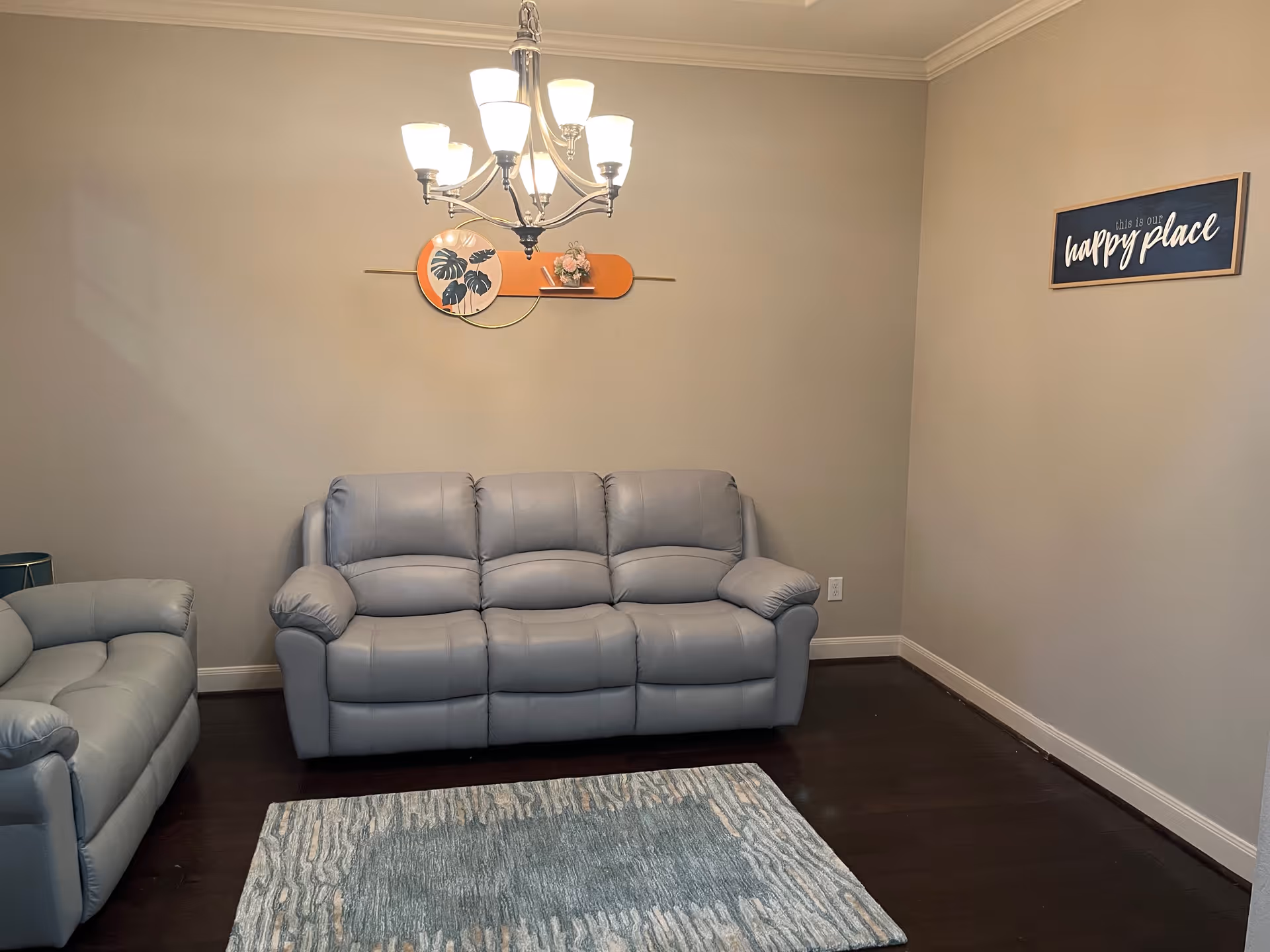 Cozy living room with gray reclining sofas, chandelier, wall art, and a blue rug.