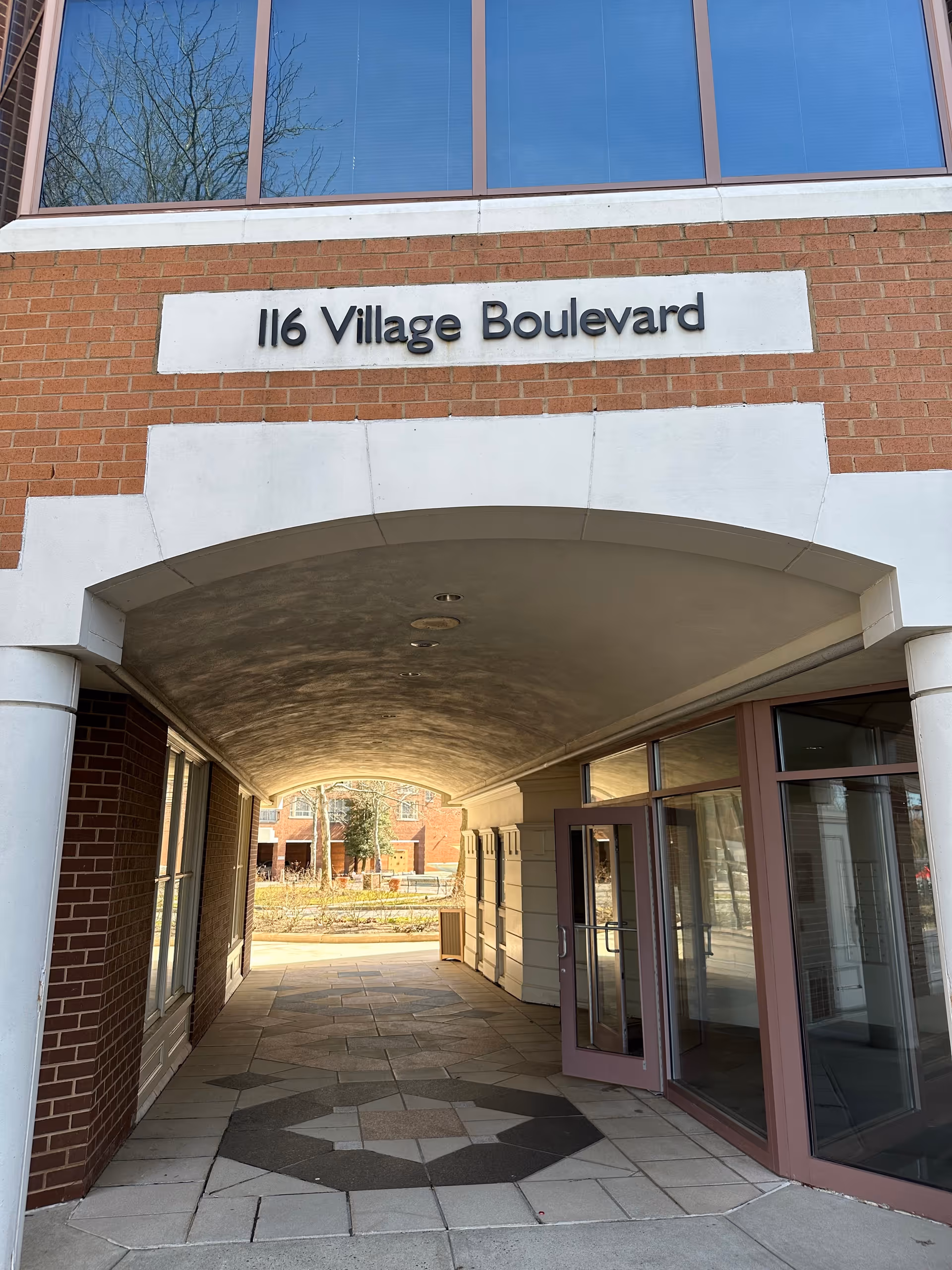 Brick building entrance with arched covered walkway and sign reading 116 Village Boulevard.