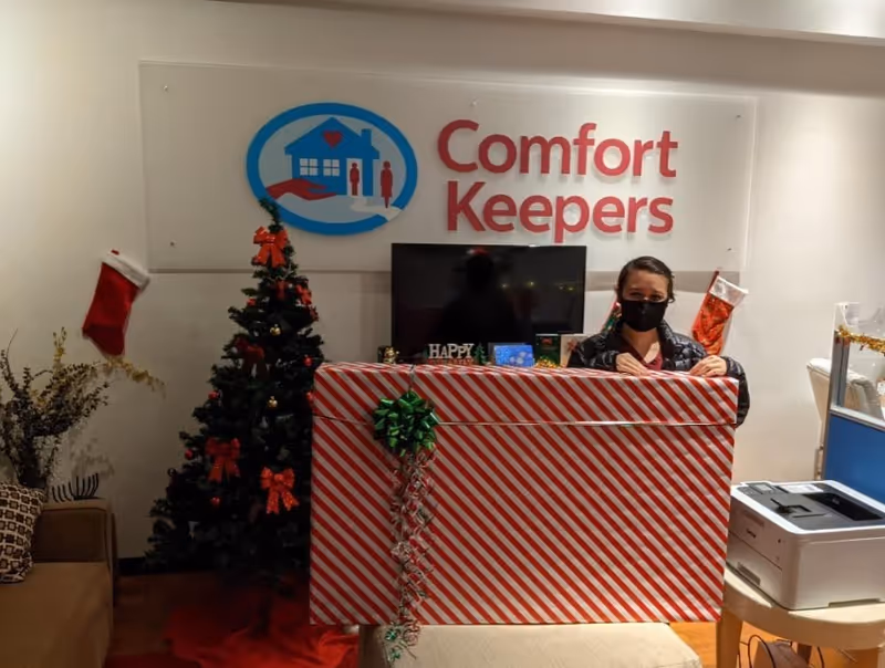 Indoor reception area with wrapped desk, Christmas tree, and a masked staff member.