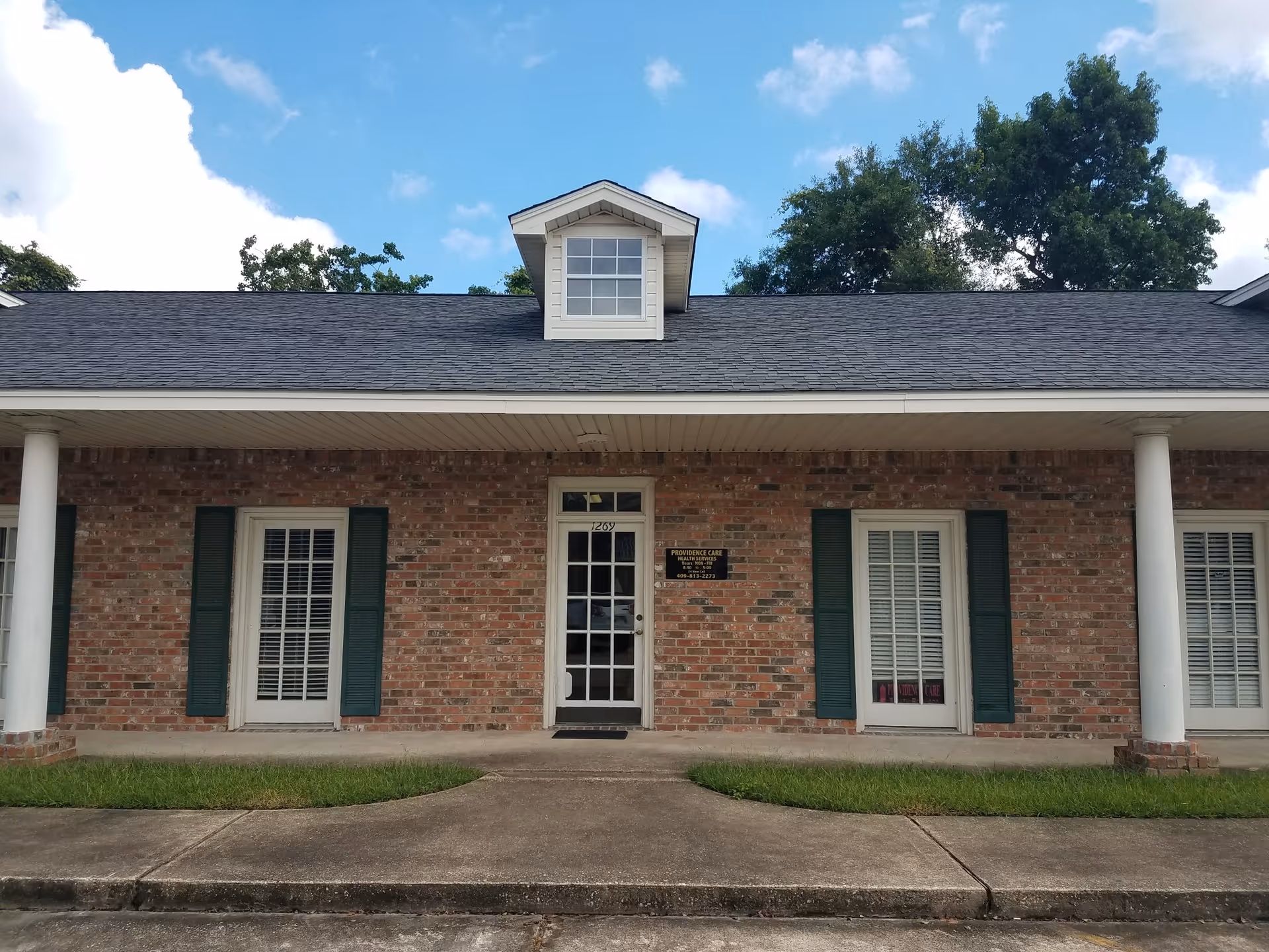 Brick, single-story facility front with central door, dormer window, and green shutters.