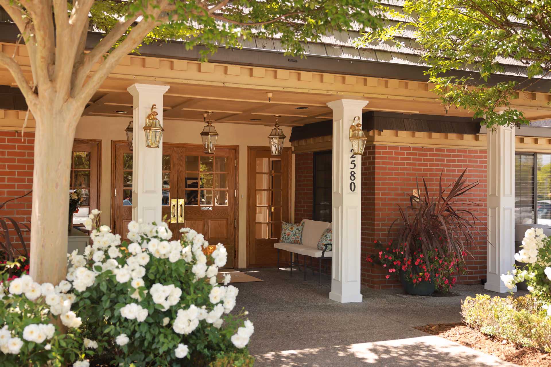 Plum Tree Care Center entrance with brick exterior, wooden doors, columns, and plants.