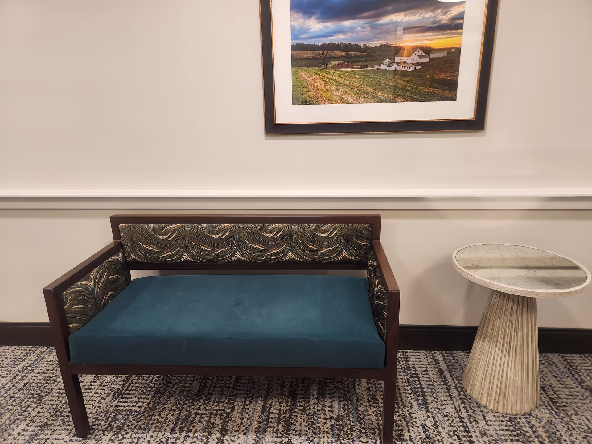Teal upholstered sofa with patterned cushions and a round marble side table in a neutral interior.