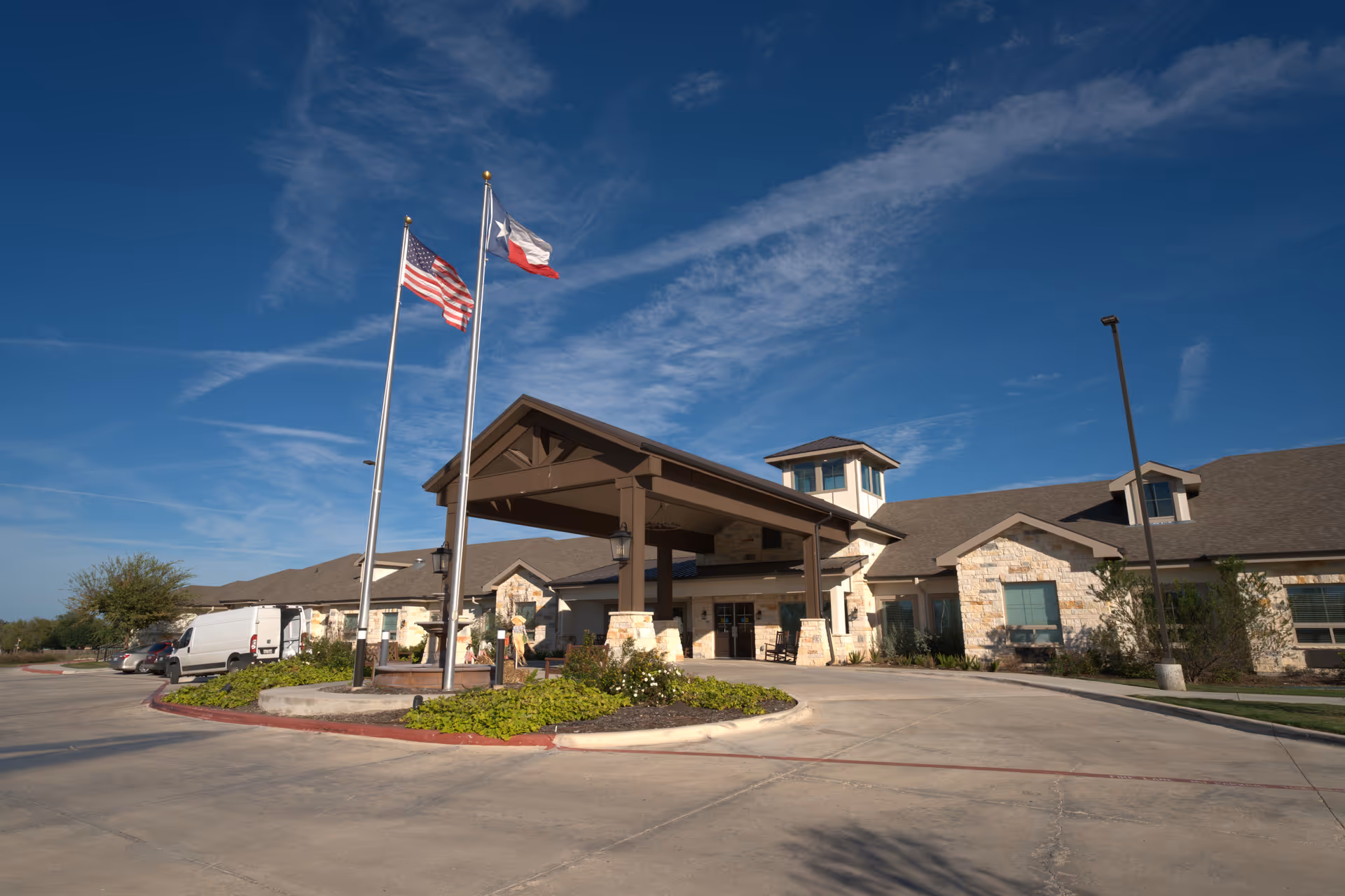 Exterior view of Volante Senior Living entrance with flagpoles and a covered driveway.