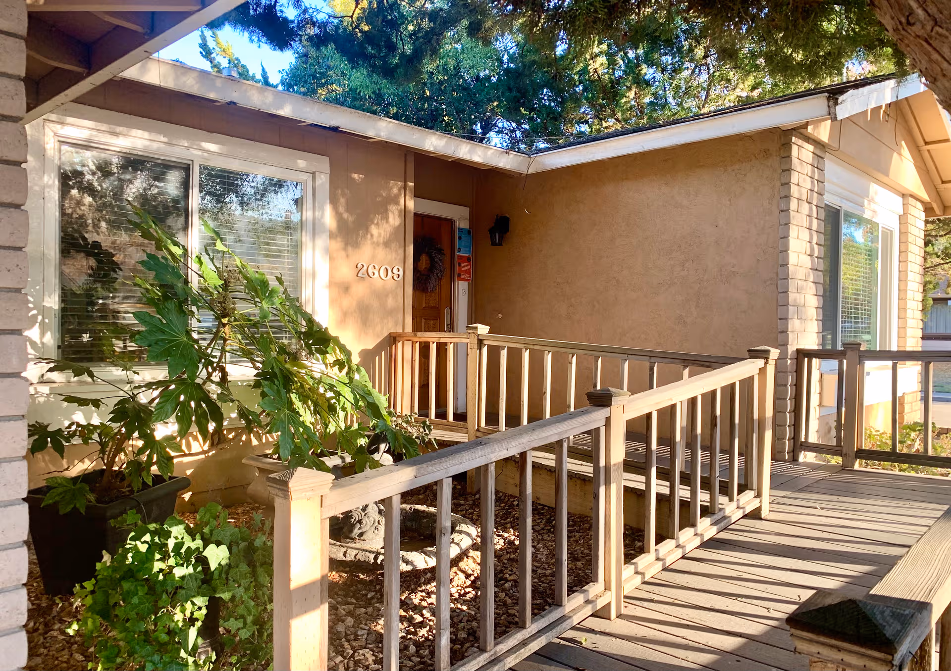 Front entrance of Pleasanton Senior Care Villa with wooden railing, potted plants, and windows.