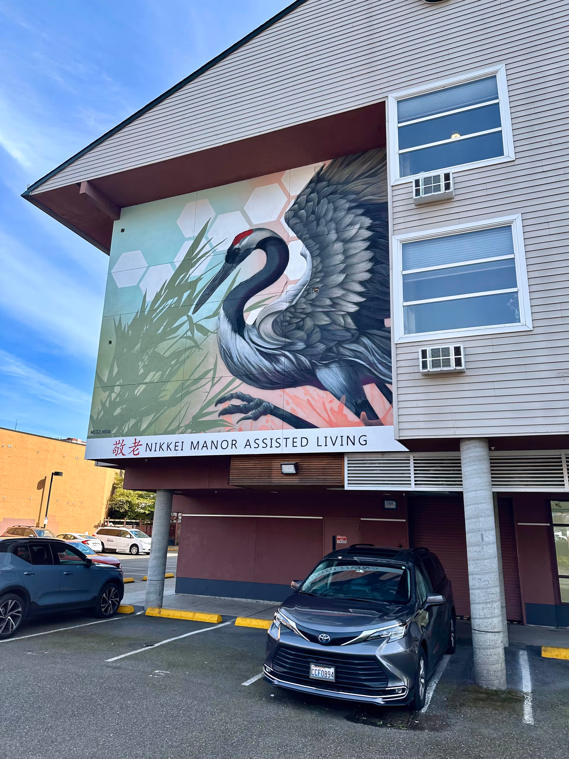 Front of a senior living building with a large swan mural and Nikkei Manor sign.