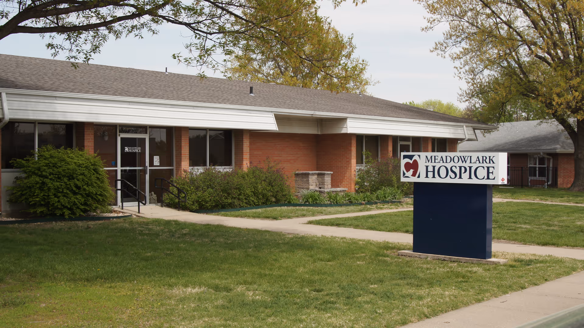 Exterior view of a brick, single-story Meadowlark Hospice building with a landscaped lawn.