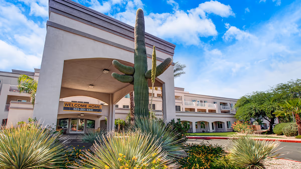 Front entrance of Holiday Vista de la Montana with a large saguaro cactus, landscaped plants, and a 'Welcome Home' banner.