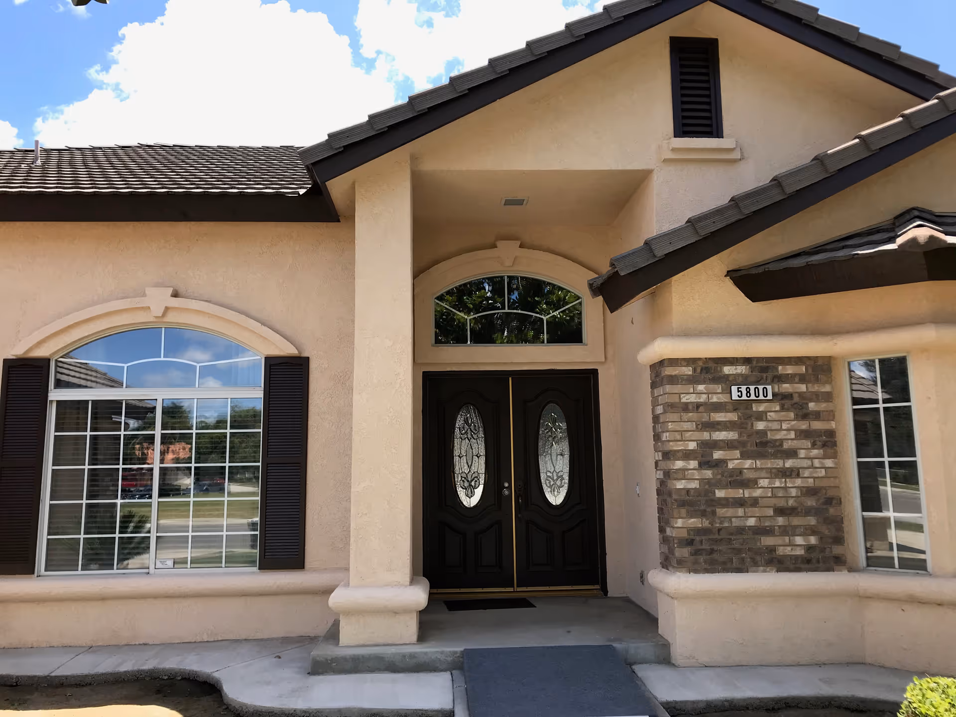 Front exterior of a beige senior living facility with arched window and double doors.