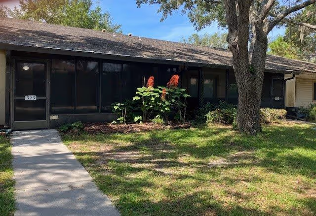 Single-story unit with a screened front porch, a concrete walkway, lawn, and a large tree.