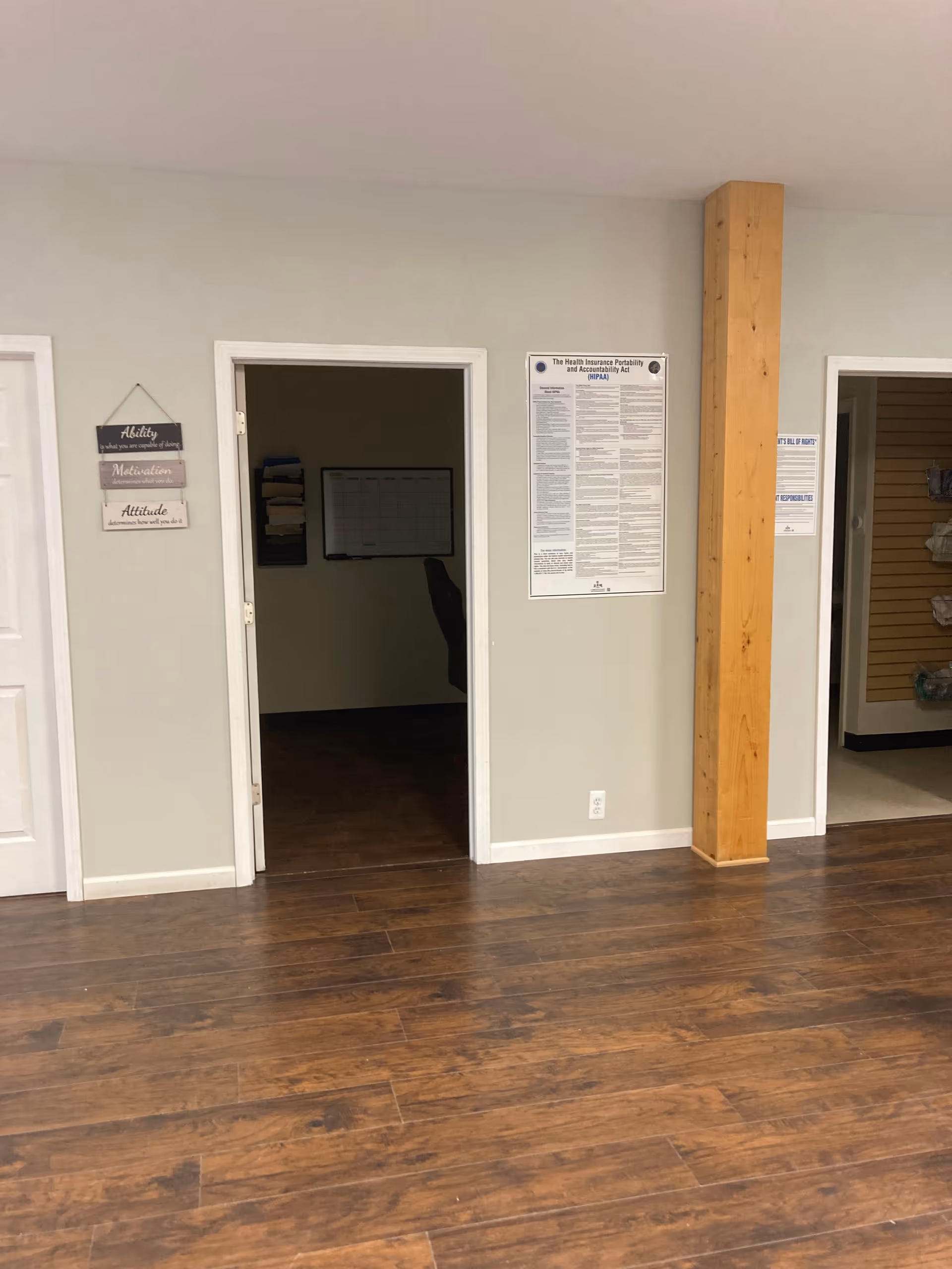 Interior hallway of a senior facility with doorways, posters, and a wooden column.