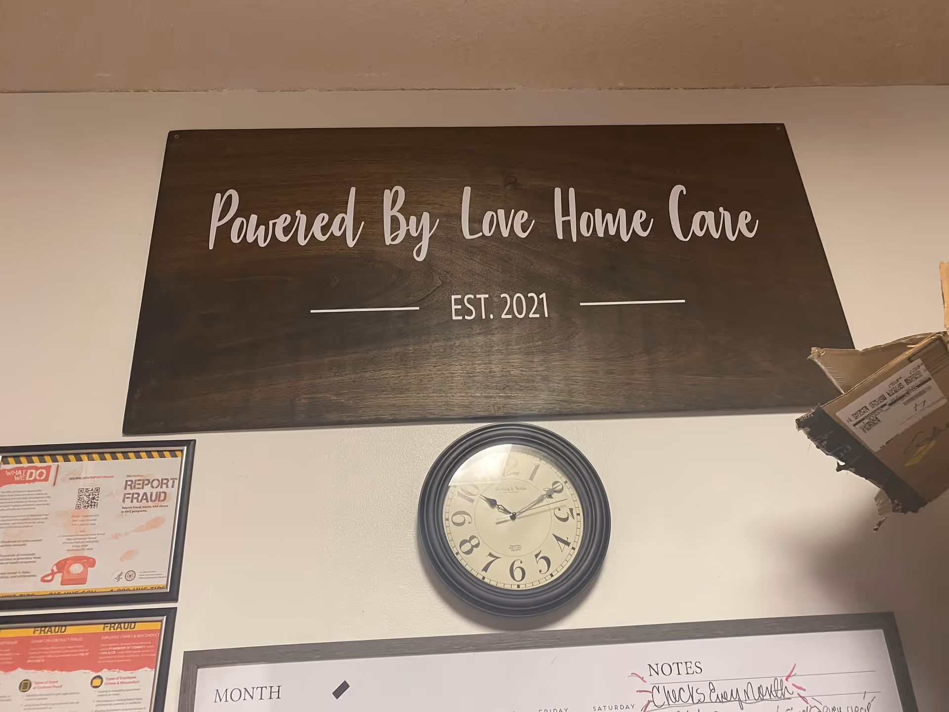 Wooden sign reading 'Powered By Love Home Care' on an interior wall with a clock underneath.