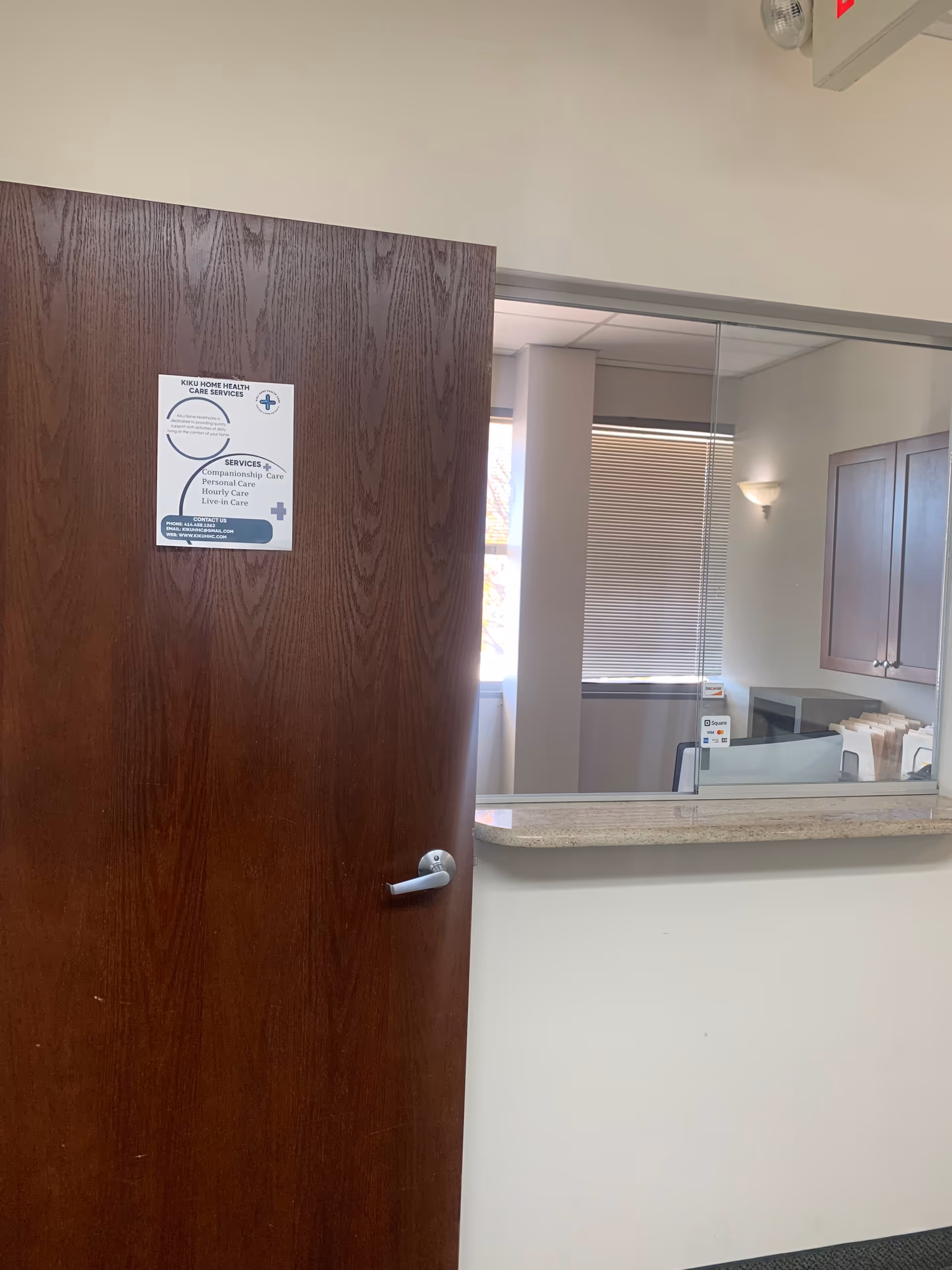 Wooden door opens to a reception counter and small office visible through glass