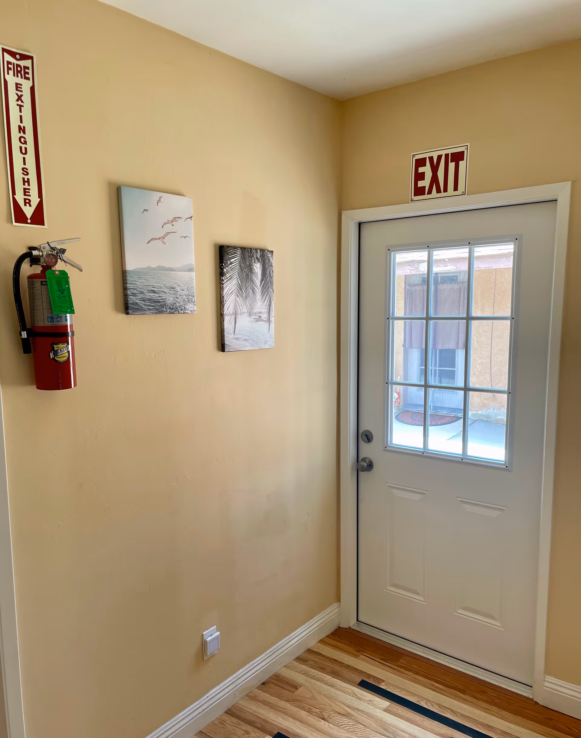 Beige hallway with exit door, fire extinguisher, and wall art.
