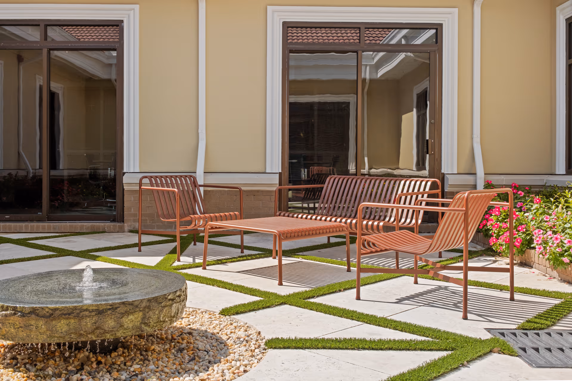 Outdoor seating area with brown metal chairs around a circular fountain in front of a building.