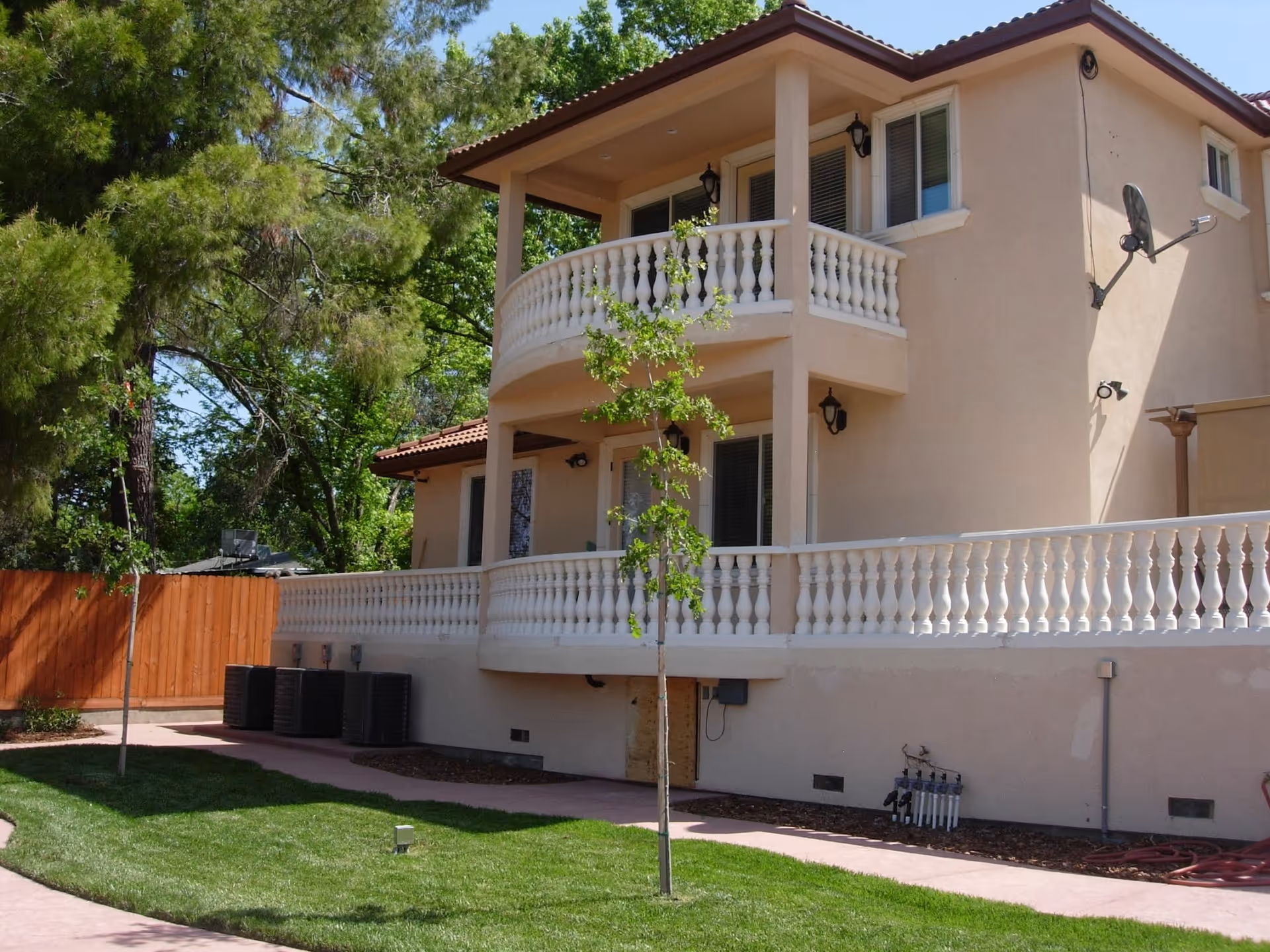 Two-story beige senior living building with white balconies and green trees in the yard.