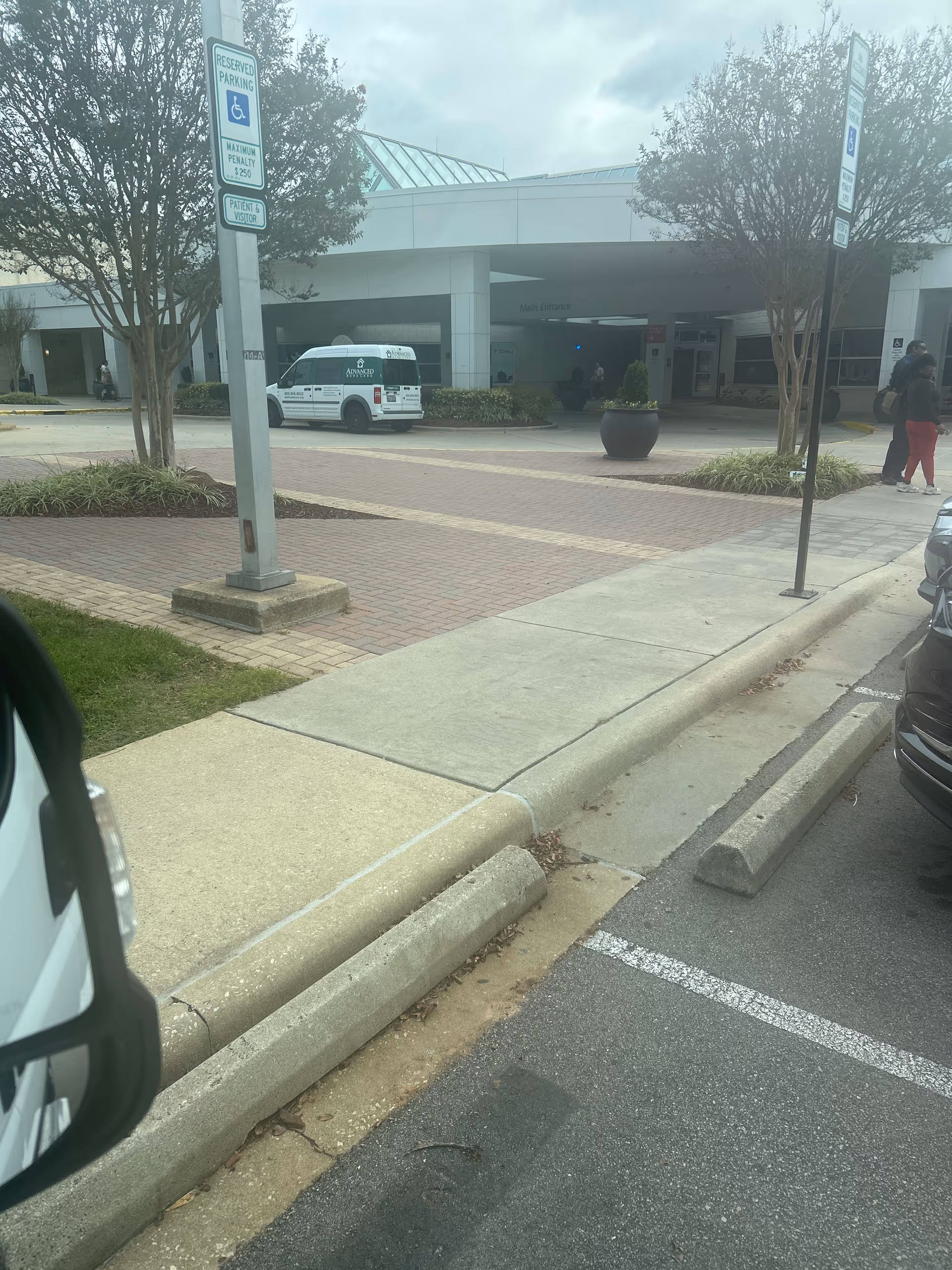 Exterior view of a senior care facility entrance with a van and pedestrians.