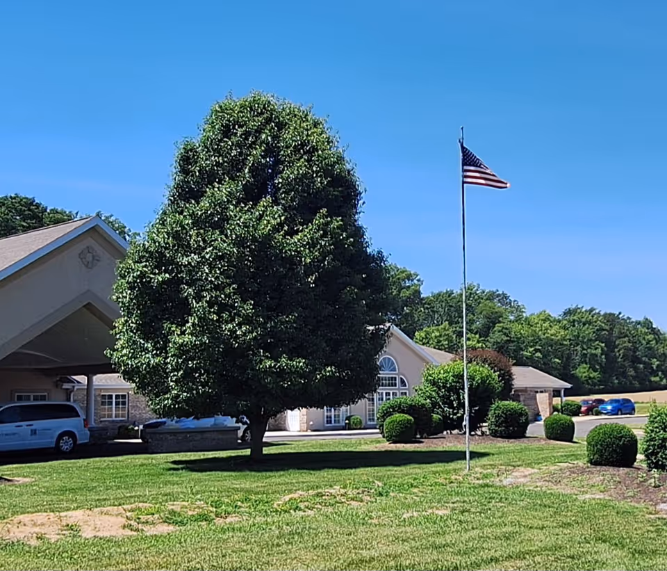Brookstone Estates of Paris exterior with flagpole, shrubs, and a large tree.
