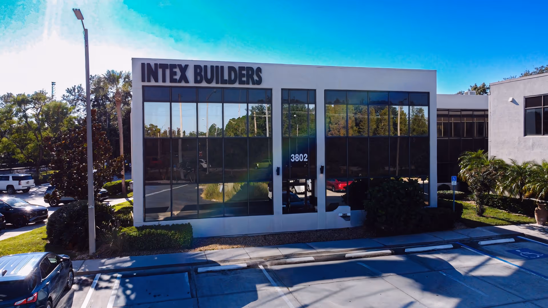 Glass-front building with INTEX BUILDERS sign and a surrounding parking lot.