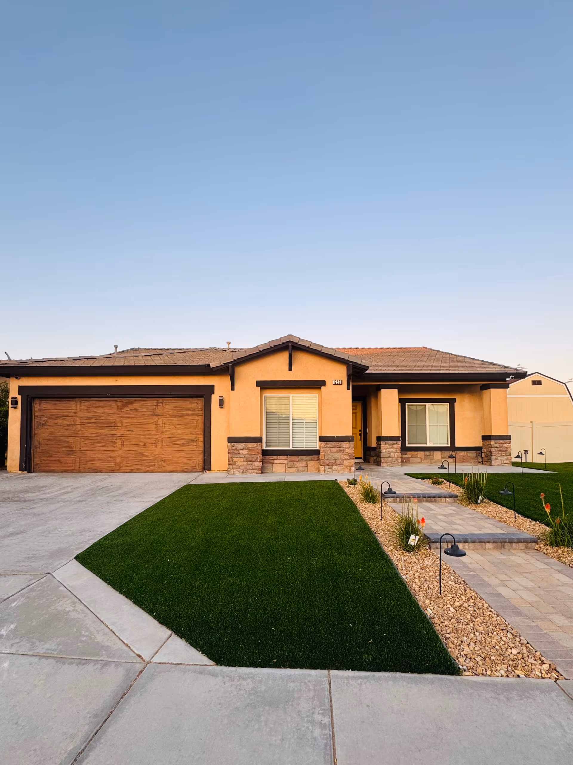 Front view of a single-story tan building with stone accents, attached garage, and landscaped walkway