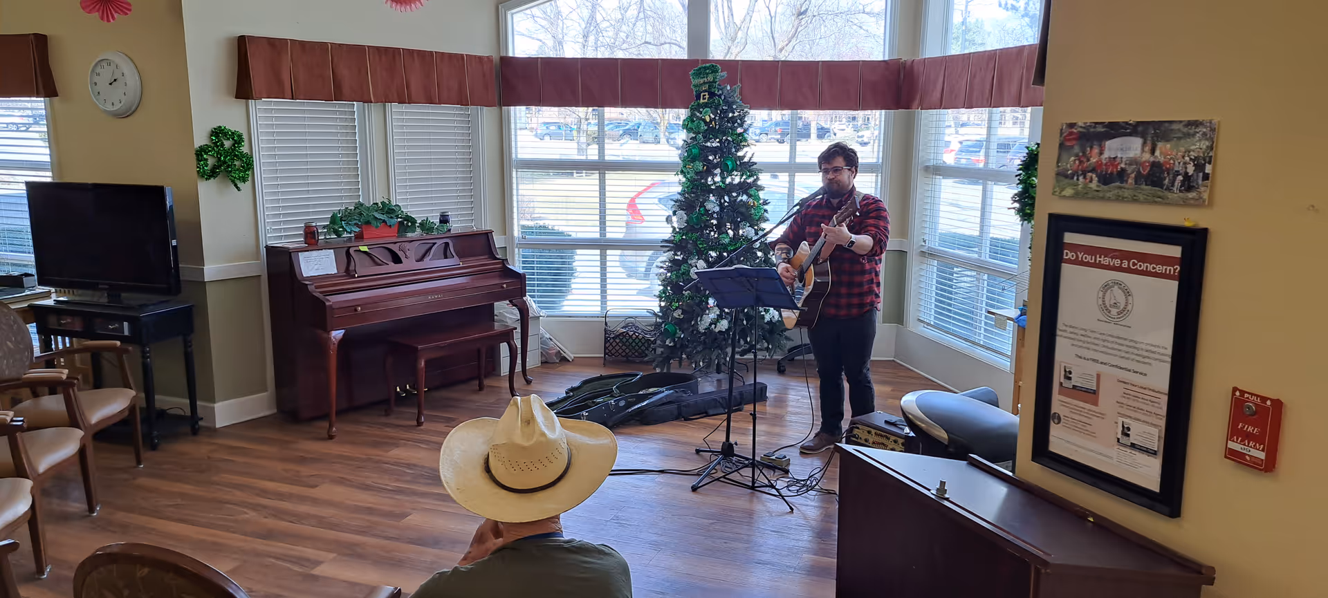 A man plays guitar in a senior living lounge beside a decorated Christmas tree.