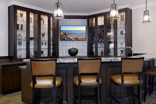 Dark wood bar with marble countertop, glass cabinets, and brown leather bar stools.