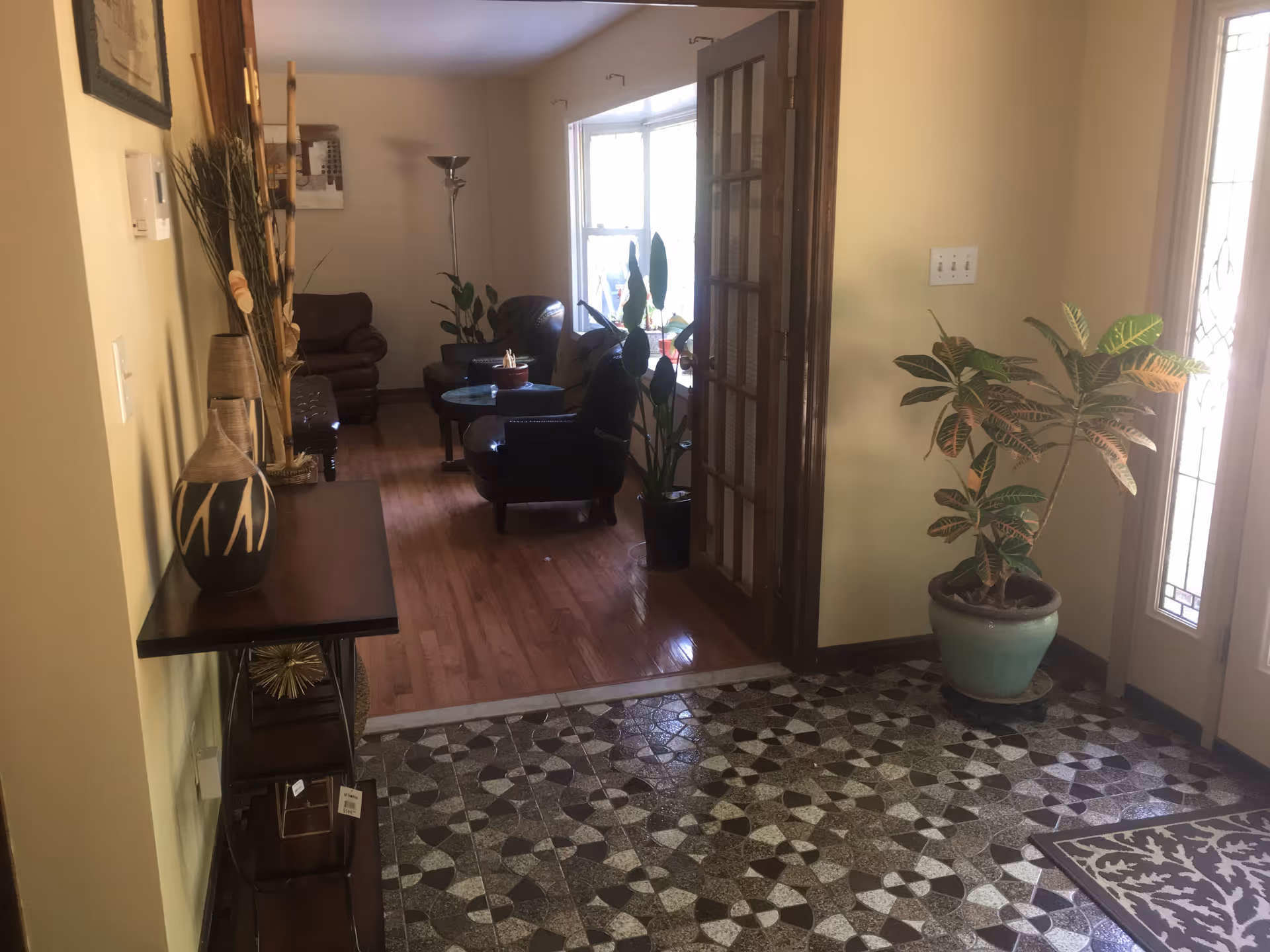 Entry foyer with tiled floor opens to a seating area and potted plants, cozy chairs visible.