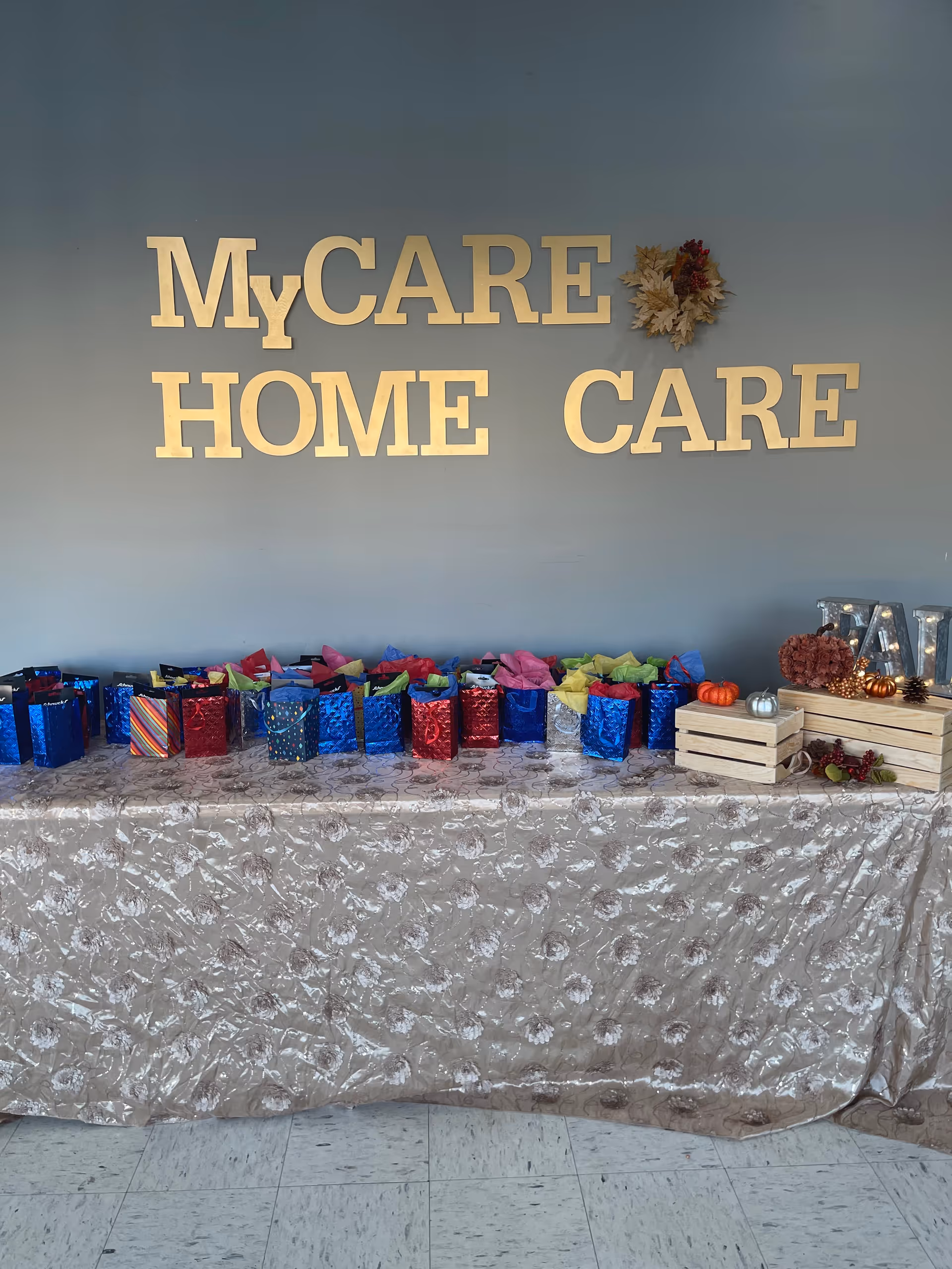 A long table with colorful gift bags sits against a blue wall reading MyCare Home Care.