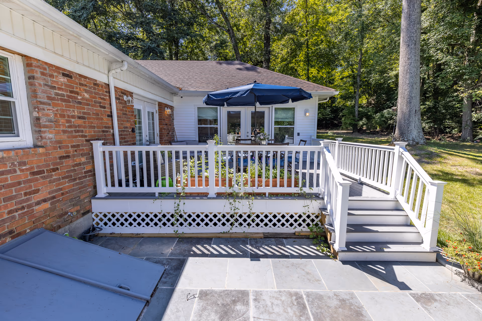 Brick home with a raised white deck, stairs, and outdoor seating under an umbrella.