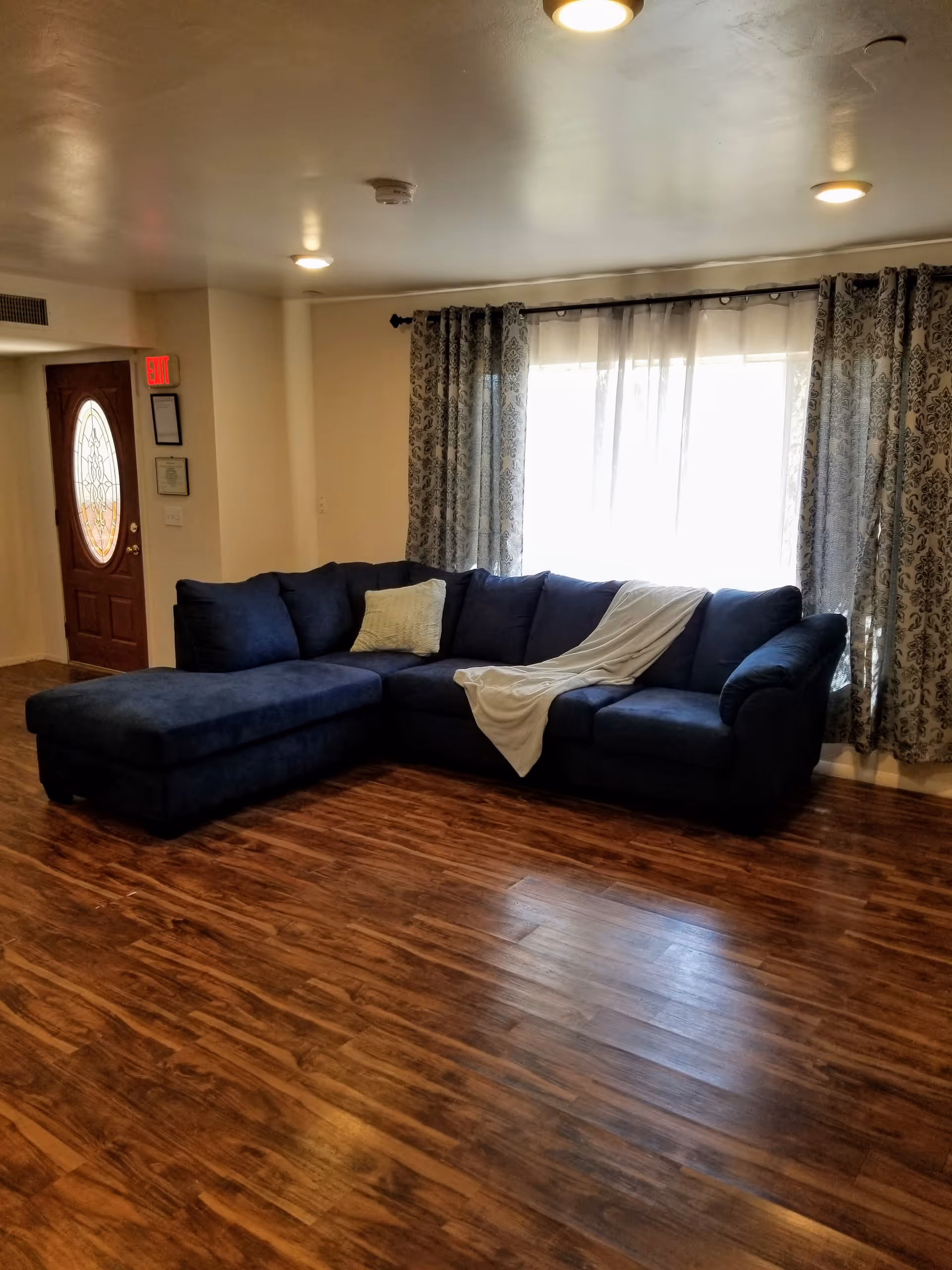 Blue sectional sofa in a spacious living room with wood floors and patterned curtains.