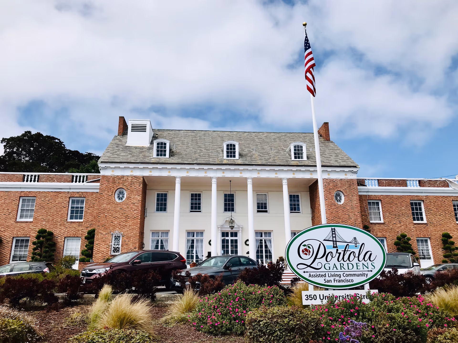 Portola Gardens assisted living building front with flagpole, sign, and landscaping.