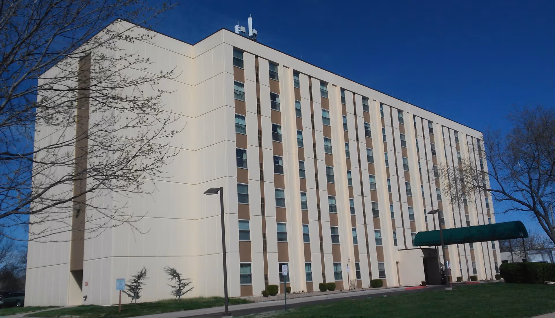 Exterior view of a tall beige senior living building with a green canopy