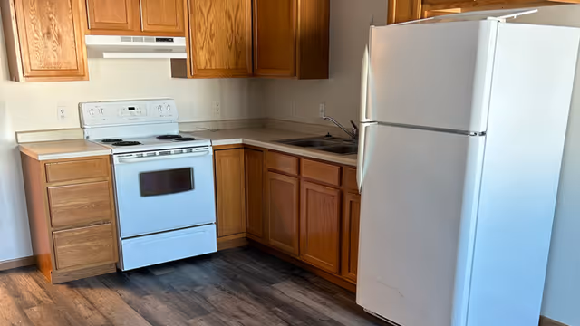 Bright kitchen with wooden cabinets, white stove, sink, and refrigerator in a senior living facility.