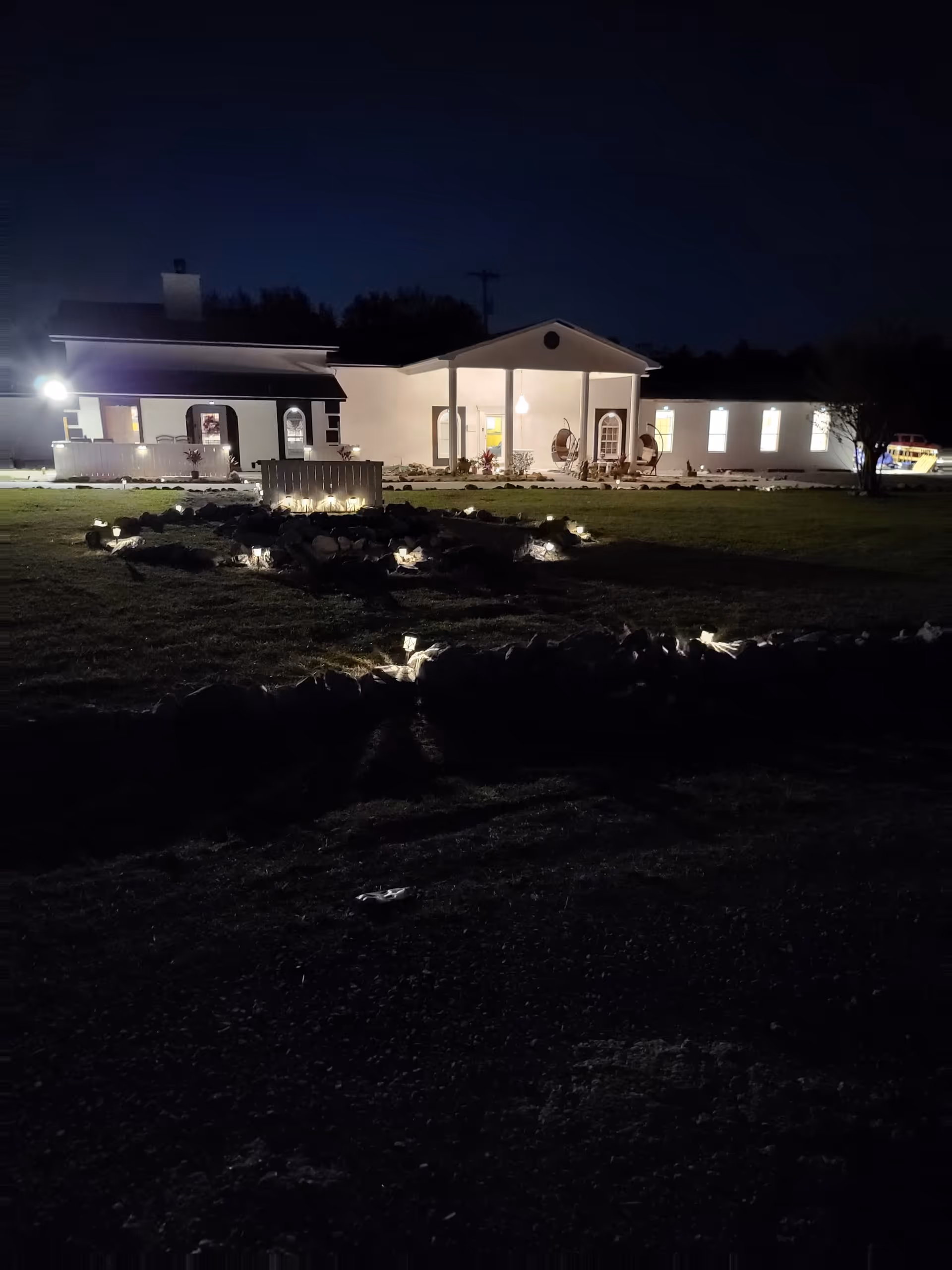 Night exterior of Timberhills LLC showing lit entrance, porch seating, and landscaped front yard.
