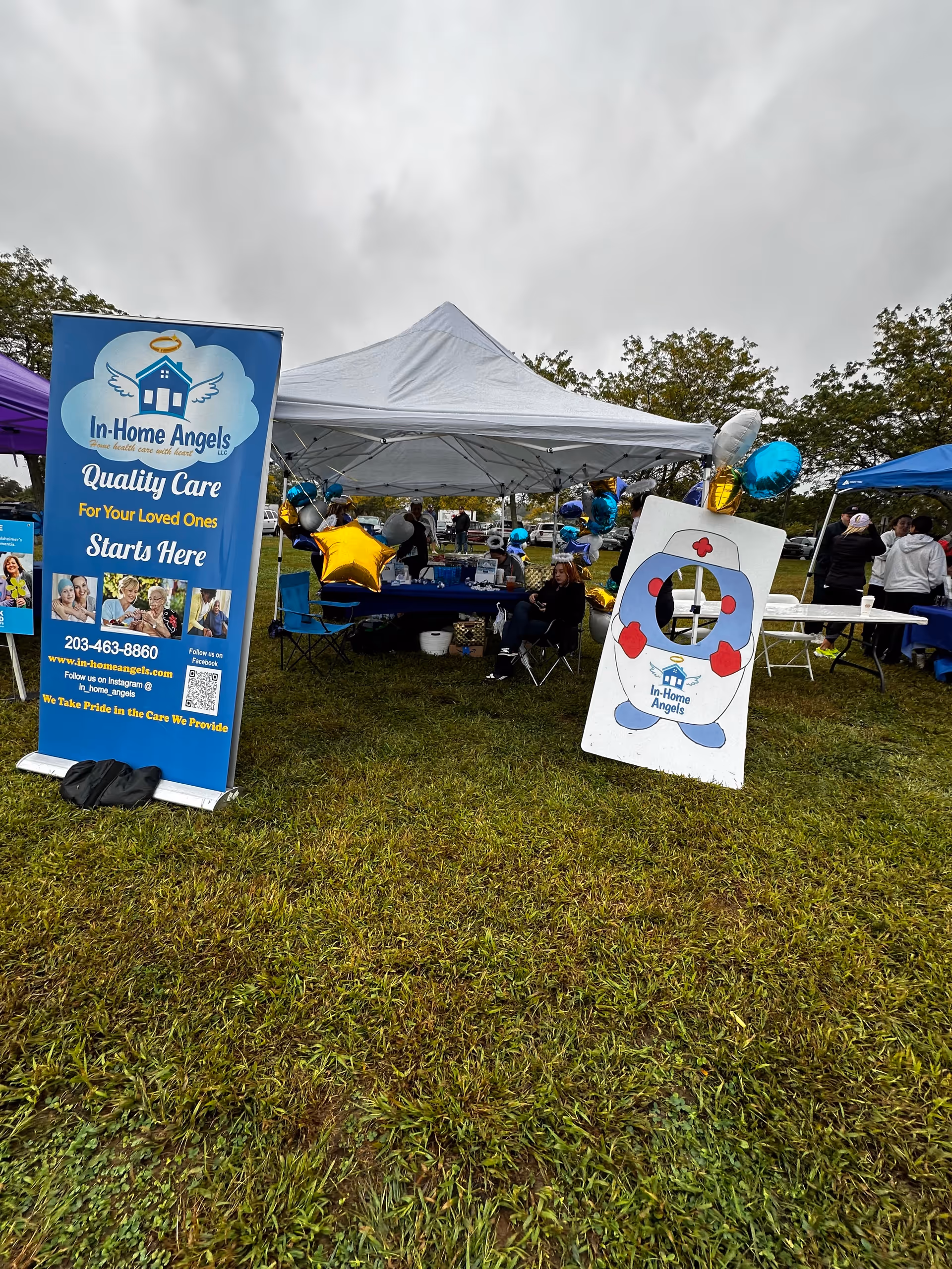 Outdoor event with tents and banners for In-Home Angels on a grassy field.