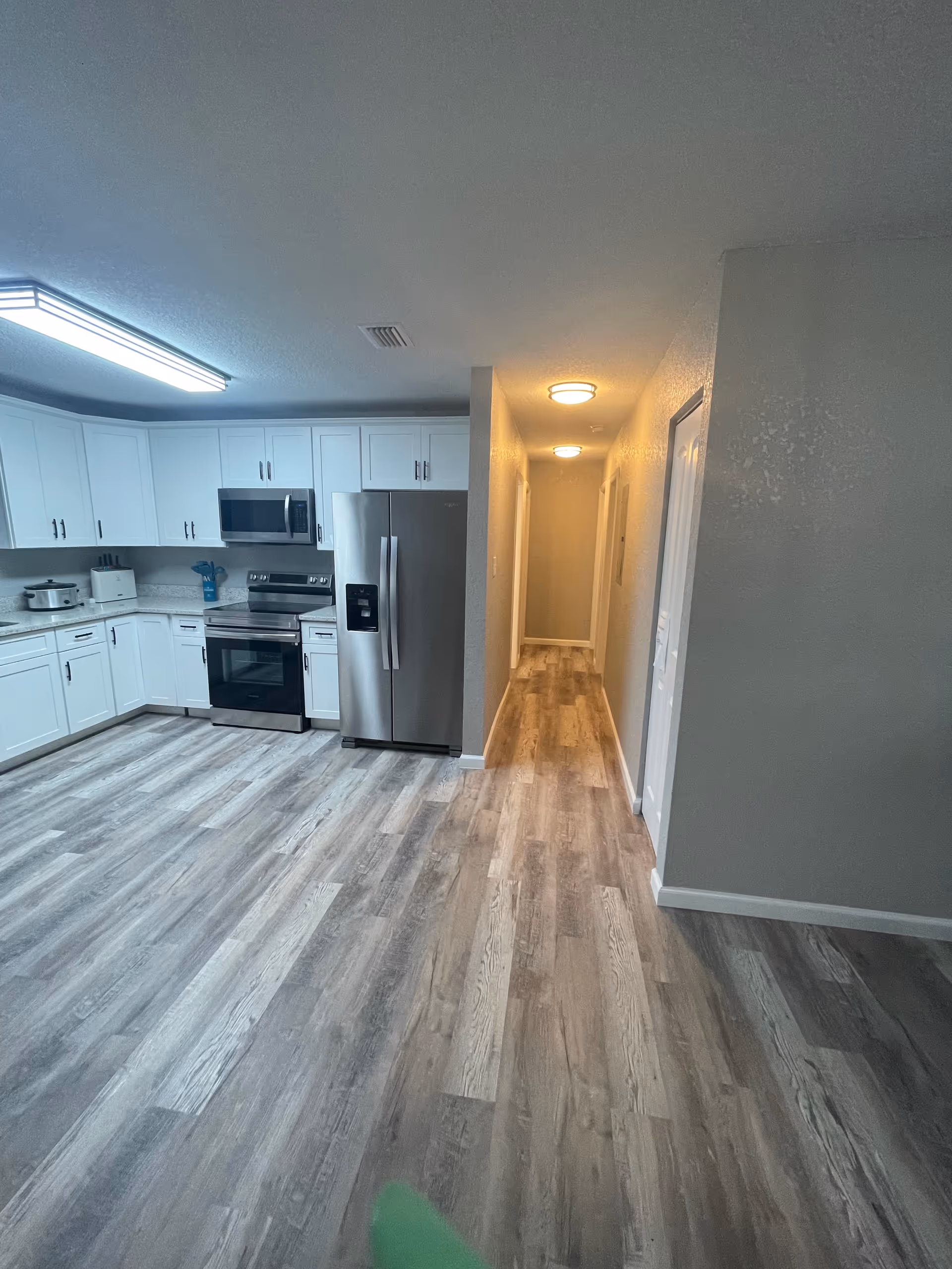Bright modern kitchen with white cabinets, stainless appliances, and a hallway leading to bedrooms.