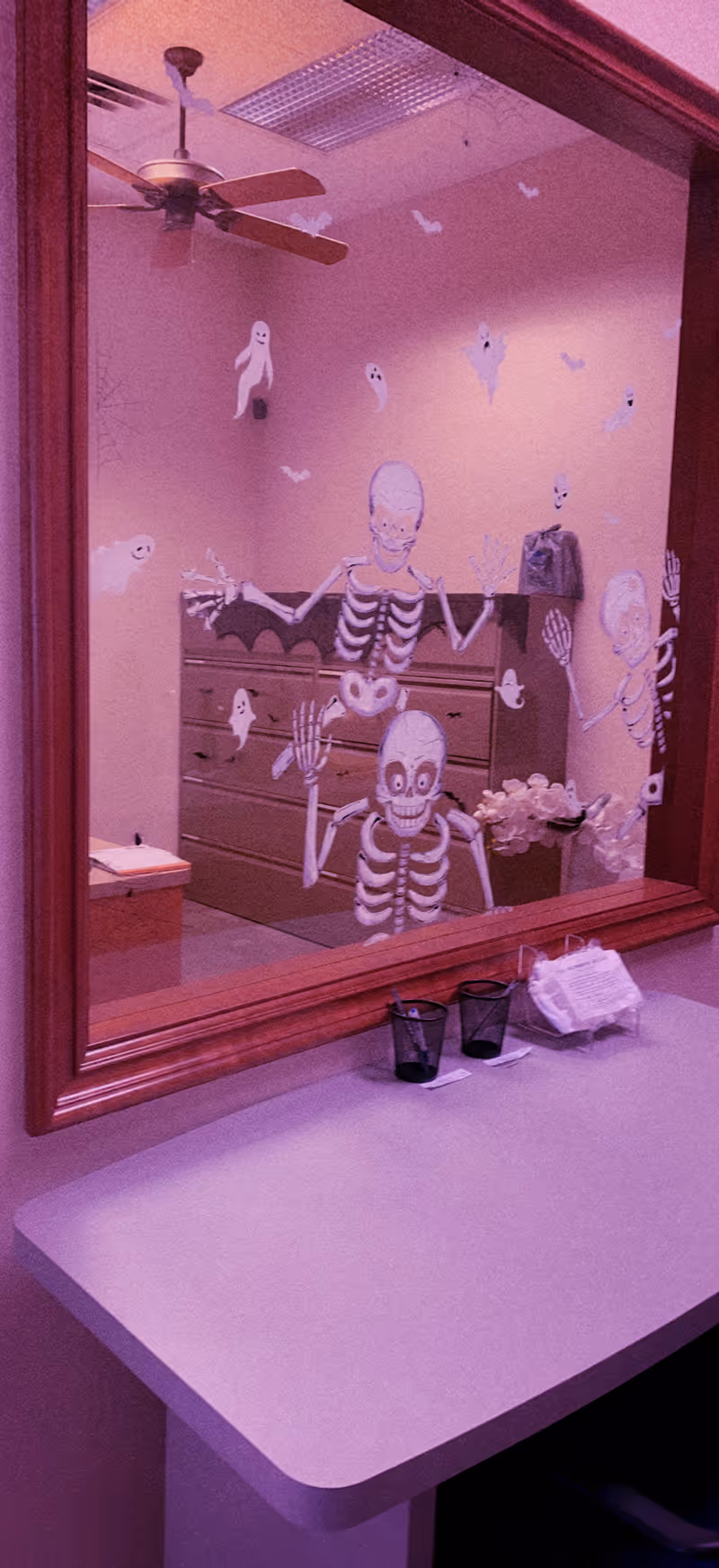 Interior of a vanity area with a mirror, skeleton decals, dresser, and pink lighting.
