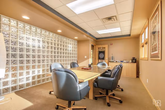Interior conference room with glass block wall, long table, rolling chairs, and coffee station.