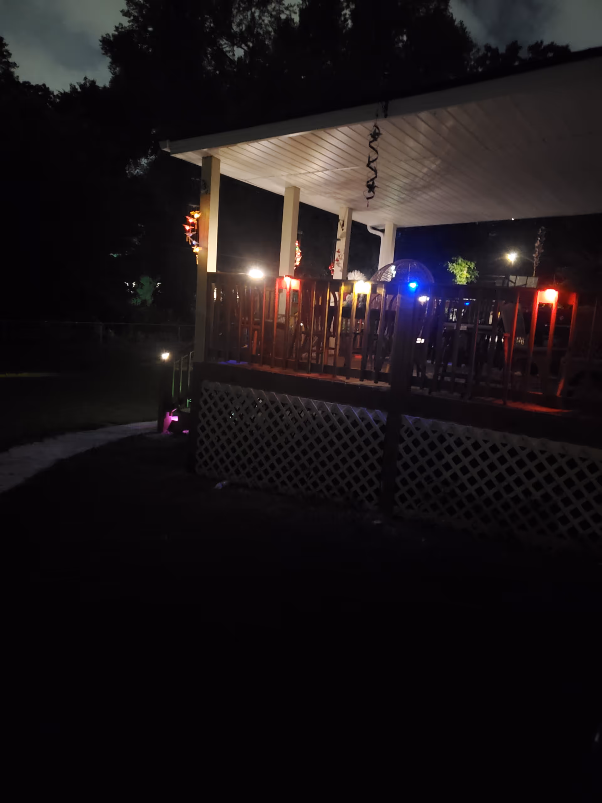 Nighttime view of a lit outdoor deck with railing and lattice skirting.